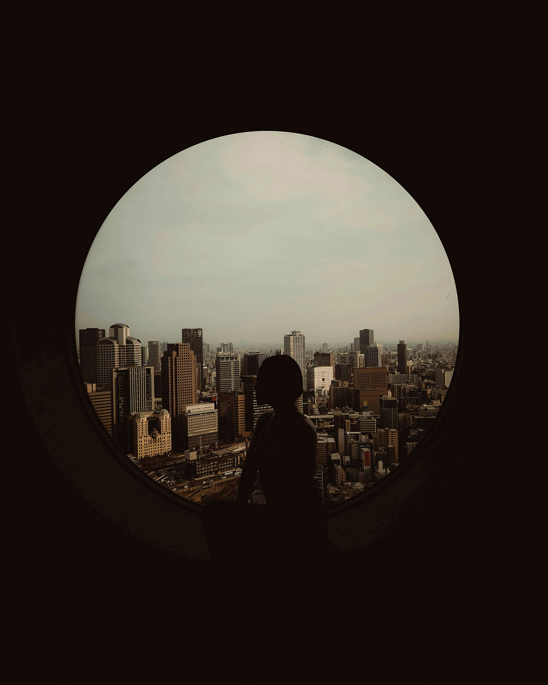 Silhuetten av en person vid ett runt fönster med utsikt över stadens skyline. (AI-genererad text)