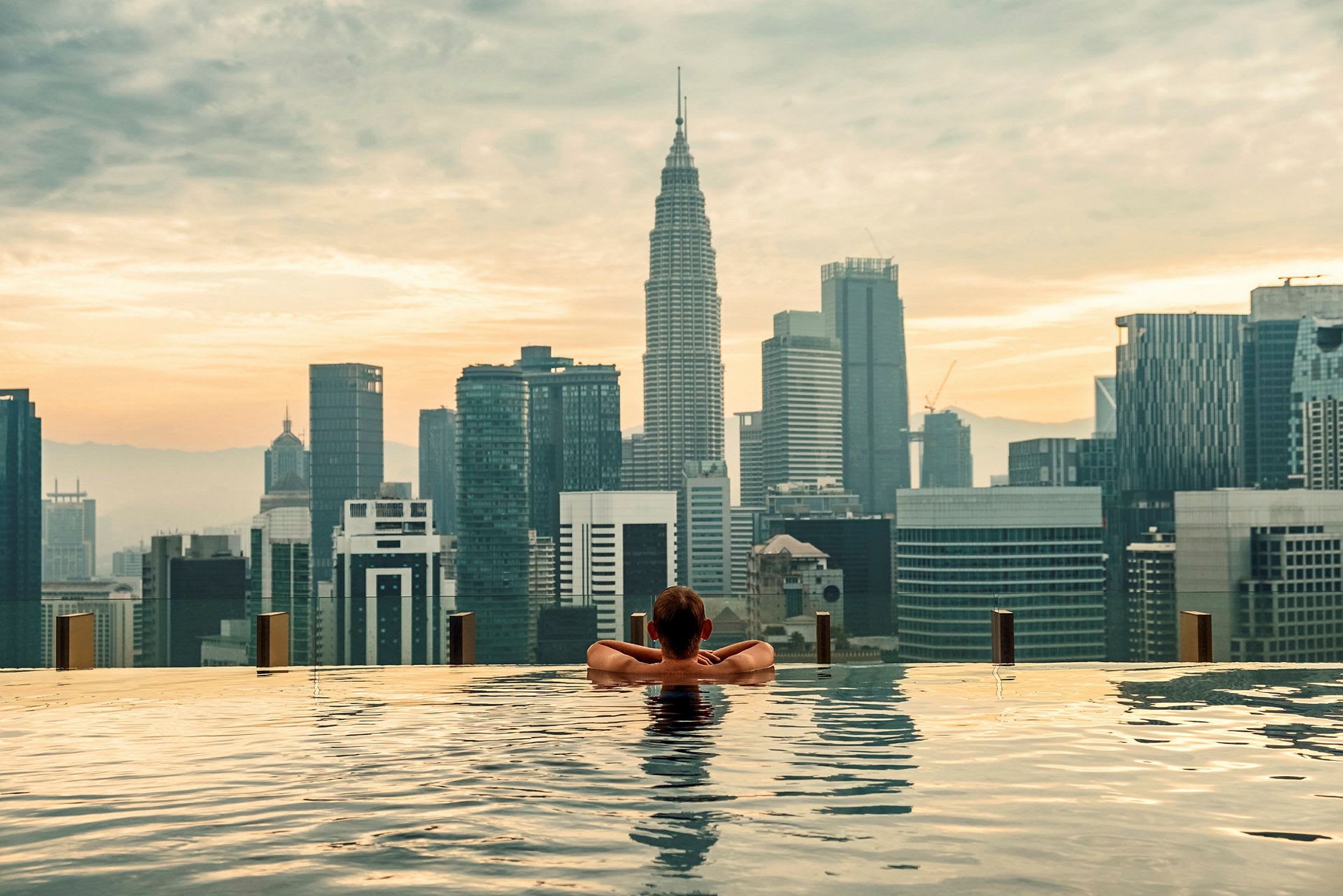 En person lutar sig mot kanten av en infinitypool med en stadssilhuett i bakgrunden. (AI-genererad text)