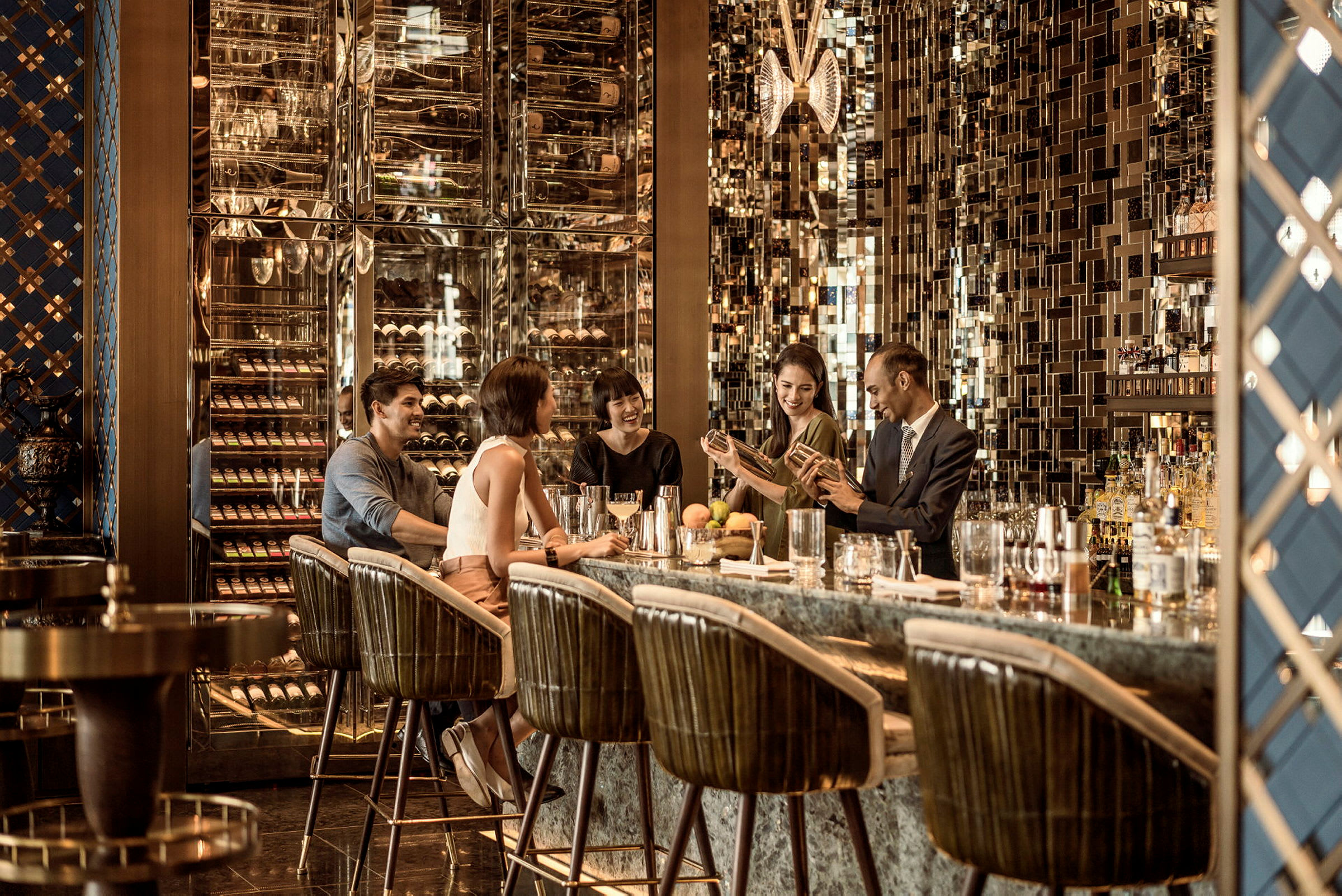 Interiör av en elegant bar med metalliska detaljer och flaskor placerade i ett stilfullt skåp. Personer sitter på barstolar vid en bardisk. (AI-genererad text)