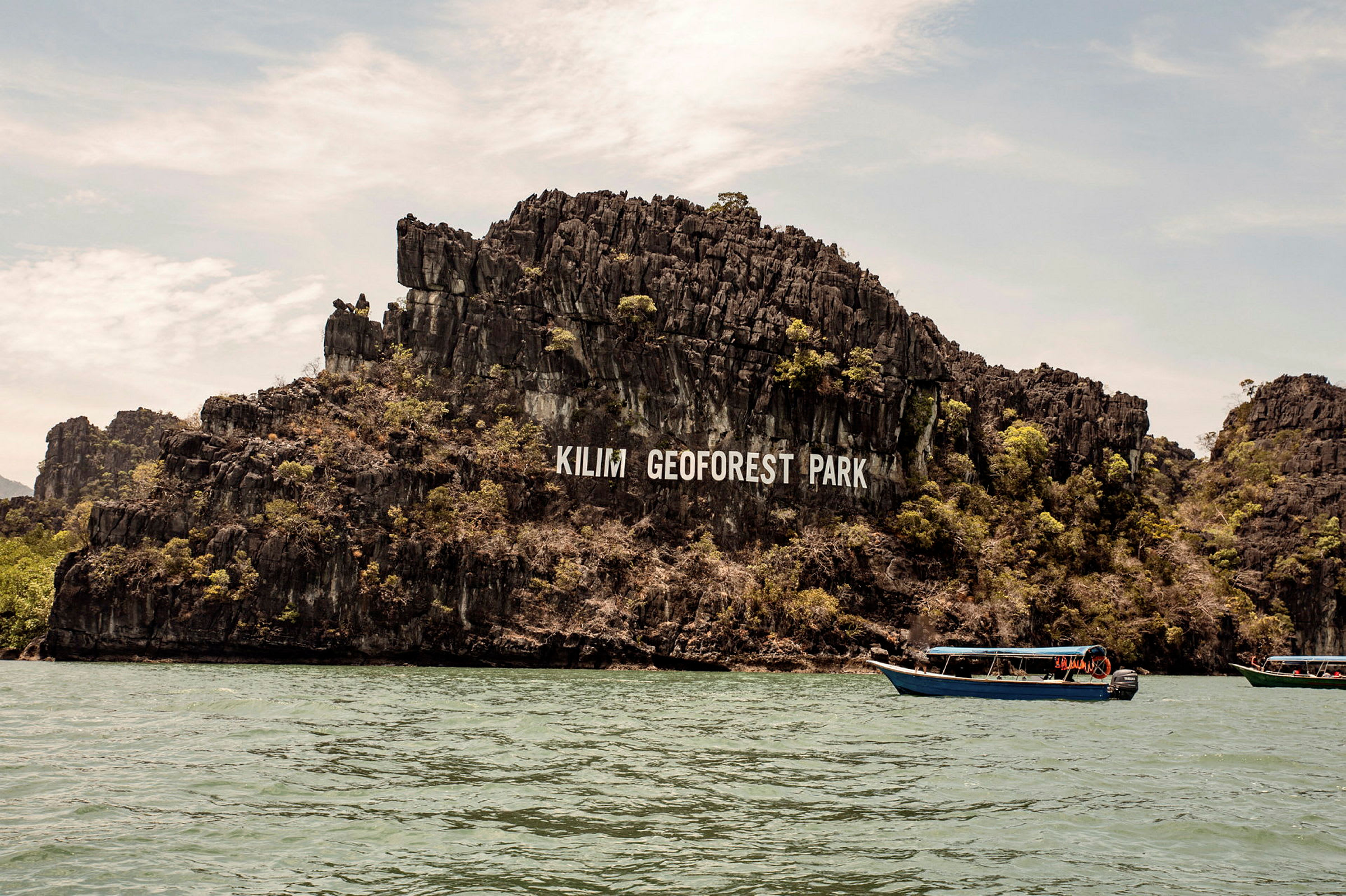 Bergsformationer med texten 'Kilim Geoforest Park' synliga. Båtar på vattnet. (AI-genererad text)