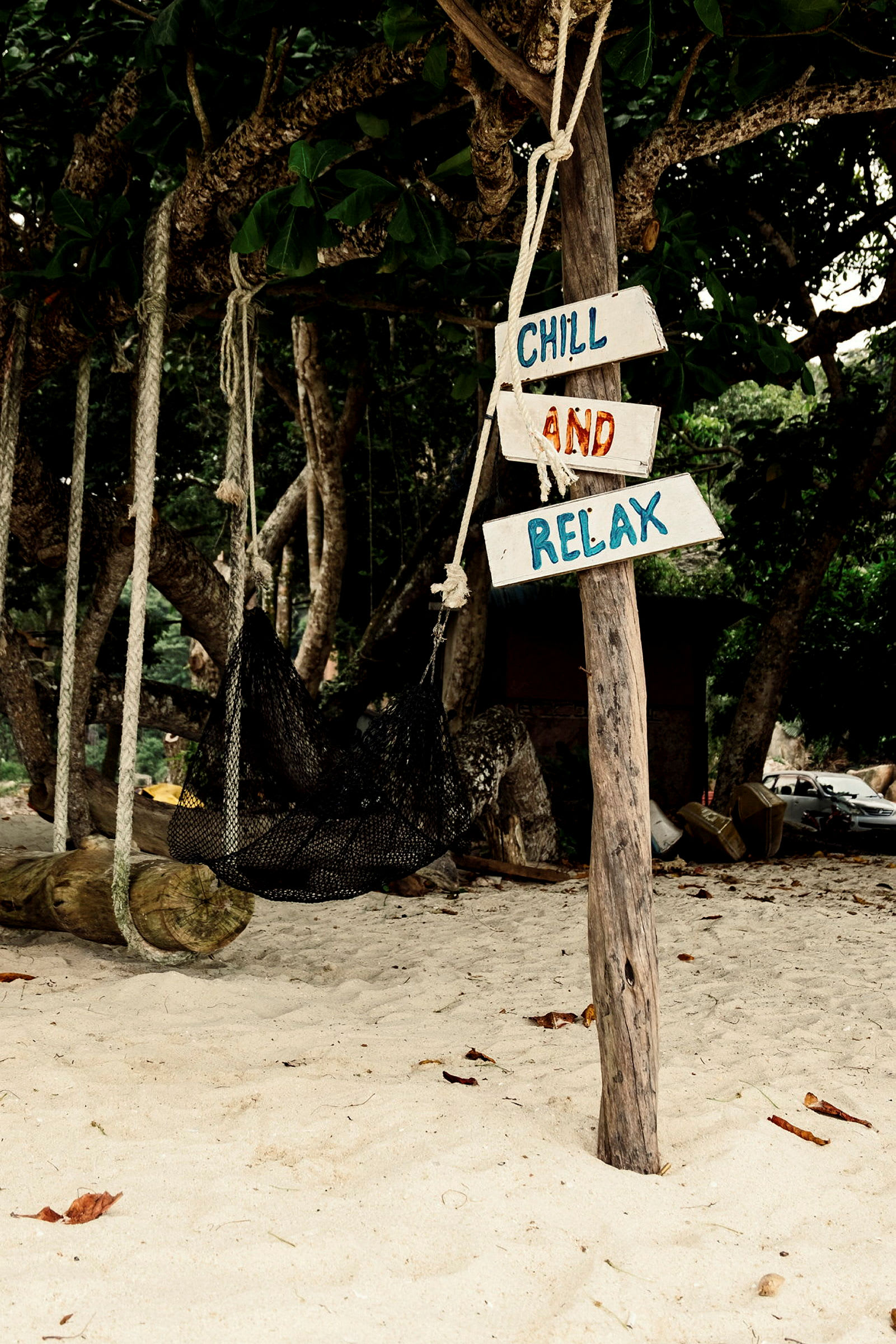 Träskylt med texten 'Chill and Relax' vid en hängmatta på en sandstrand. (AI-genererad text)