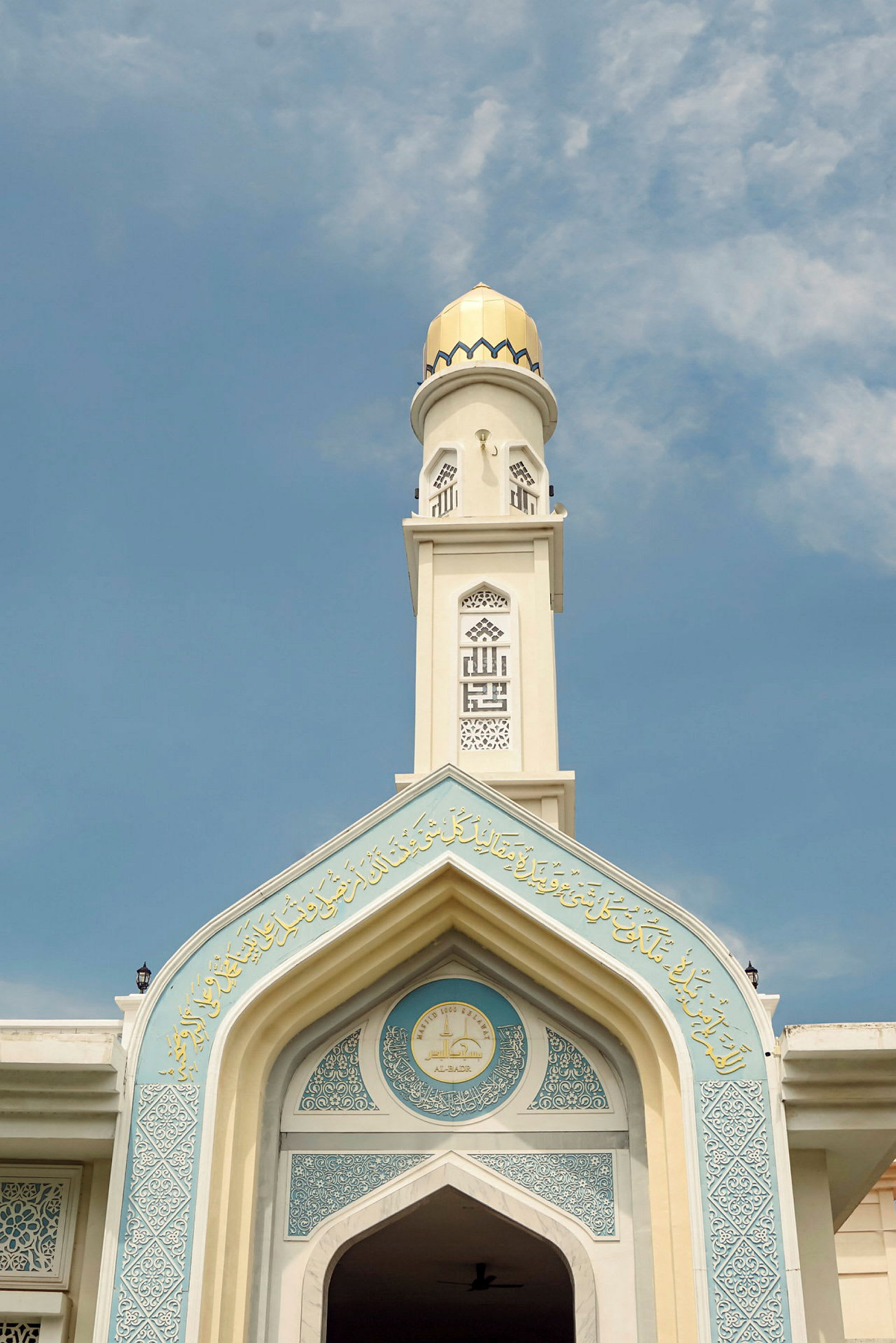 Vit minaret med ornament och guldkupol mot blå himmel. (AI-genererad text)