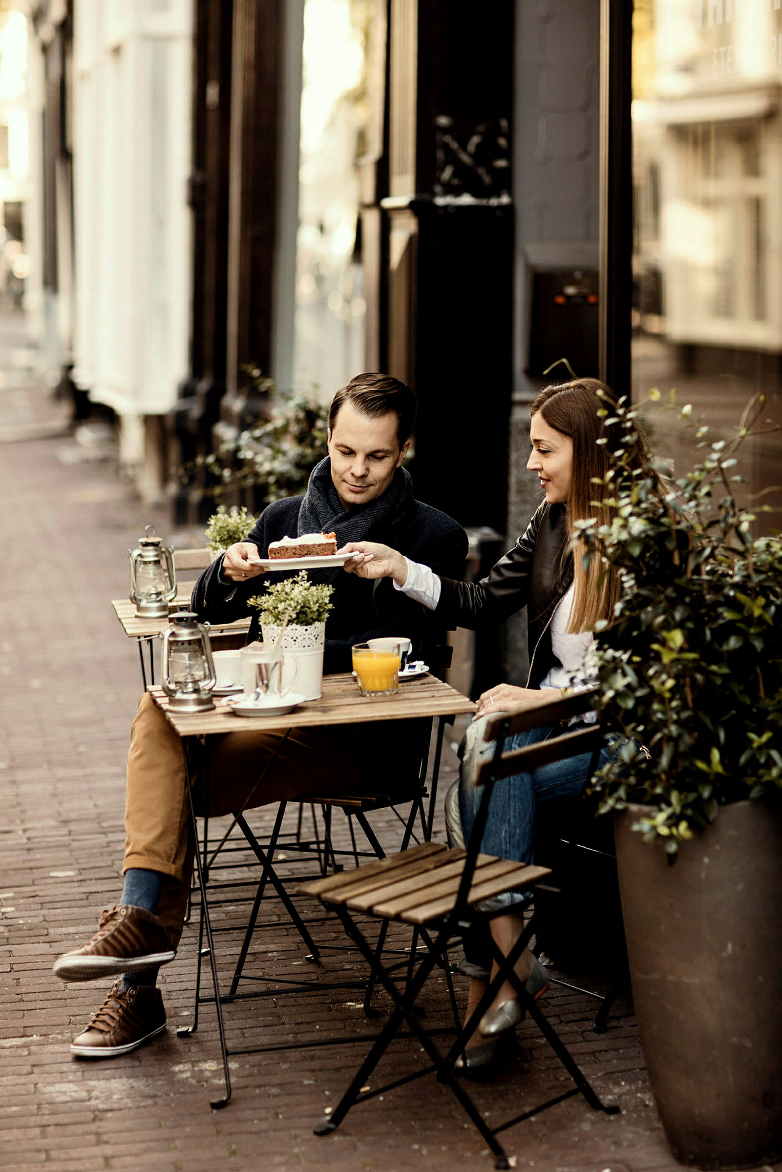 Två personer sitter vid ett cafébord utomhus med drycker och bakverk. (AI-genererad text)