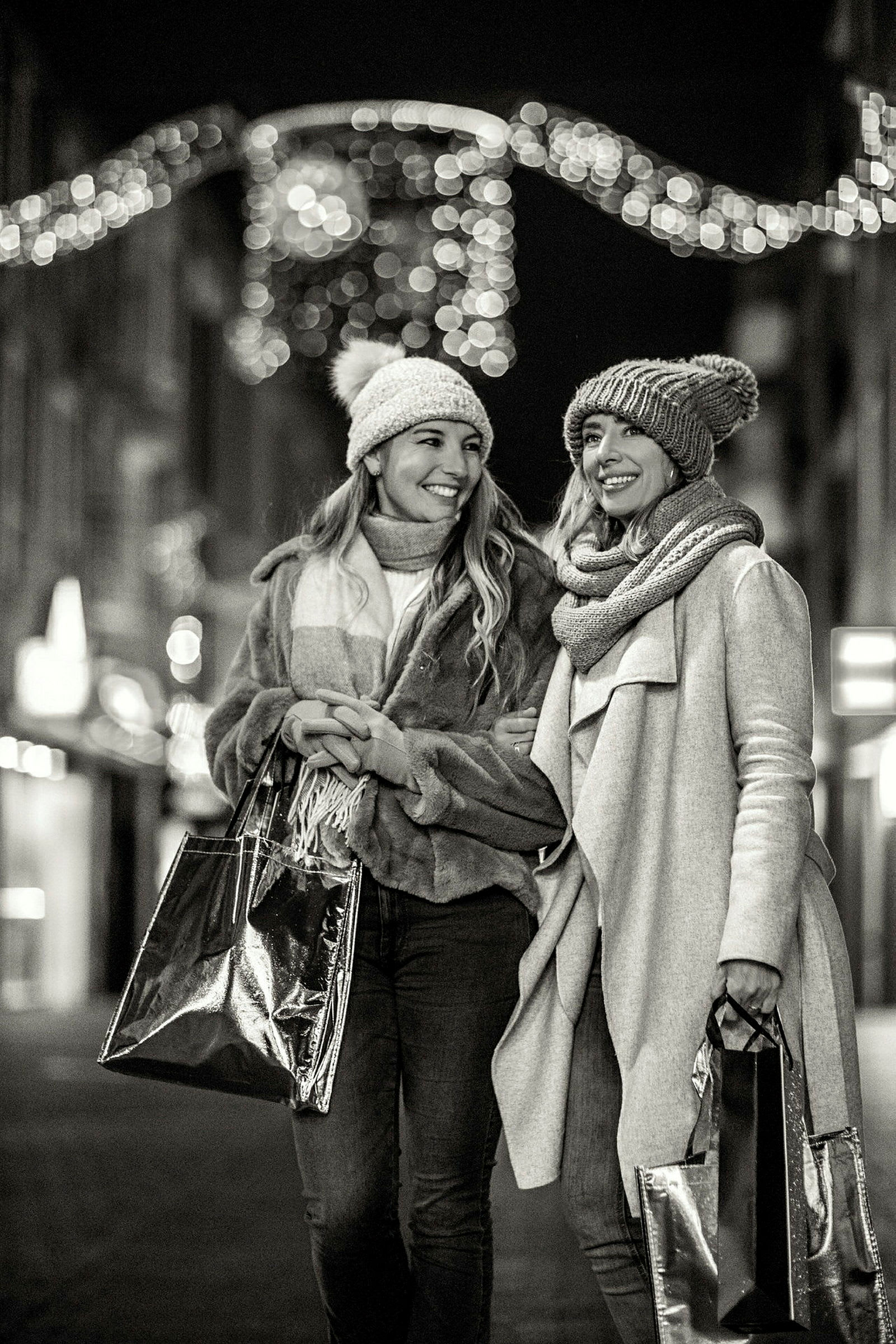 Två personer går på en gata med shoppingpåsar, omgivna av festlig belysning. (AI-genererad text)
