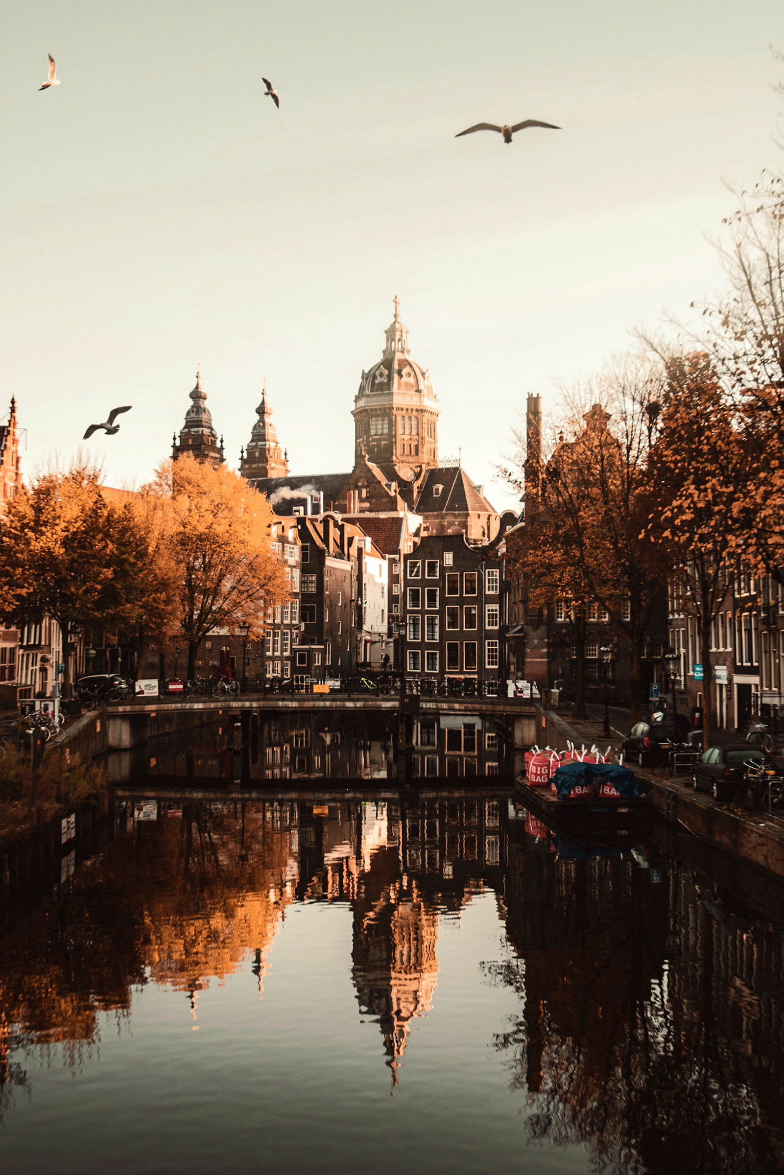 Vy över en kanal i Amsterdam med byggnader och kyrktorn i bakgrunden. (AI-genererad text)