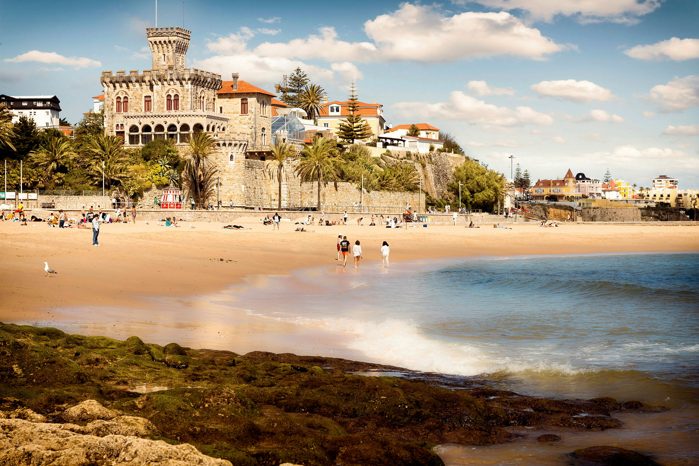 Strand med vågor i förgrunden och byggnader i bakgrunden. (AI-genererad text)