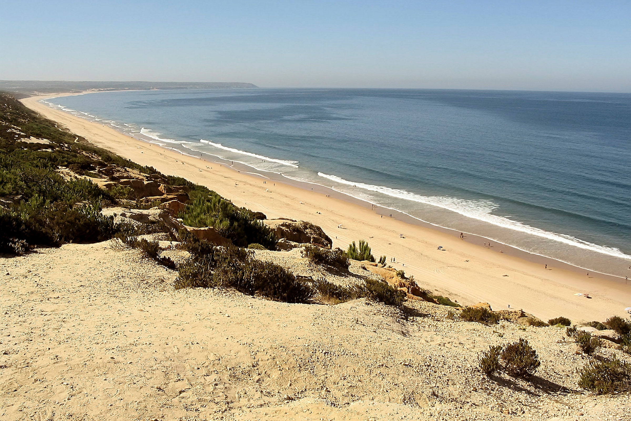 En vidsträckt sandstrand vid havet med vågor som slår mot strandkanten. (AI-genererad text)