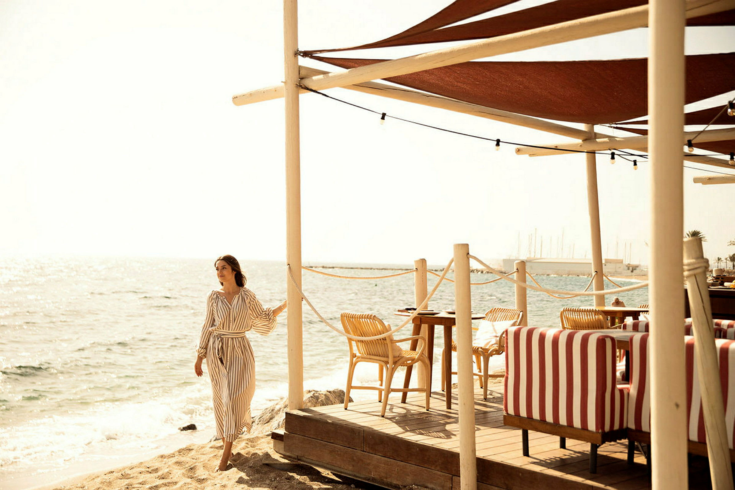 Sandstrand vid havet med uteservering och röda och vita randiga soffor. (AI-genererad text)