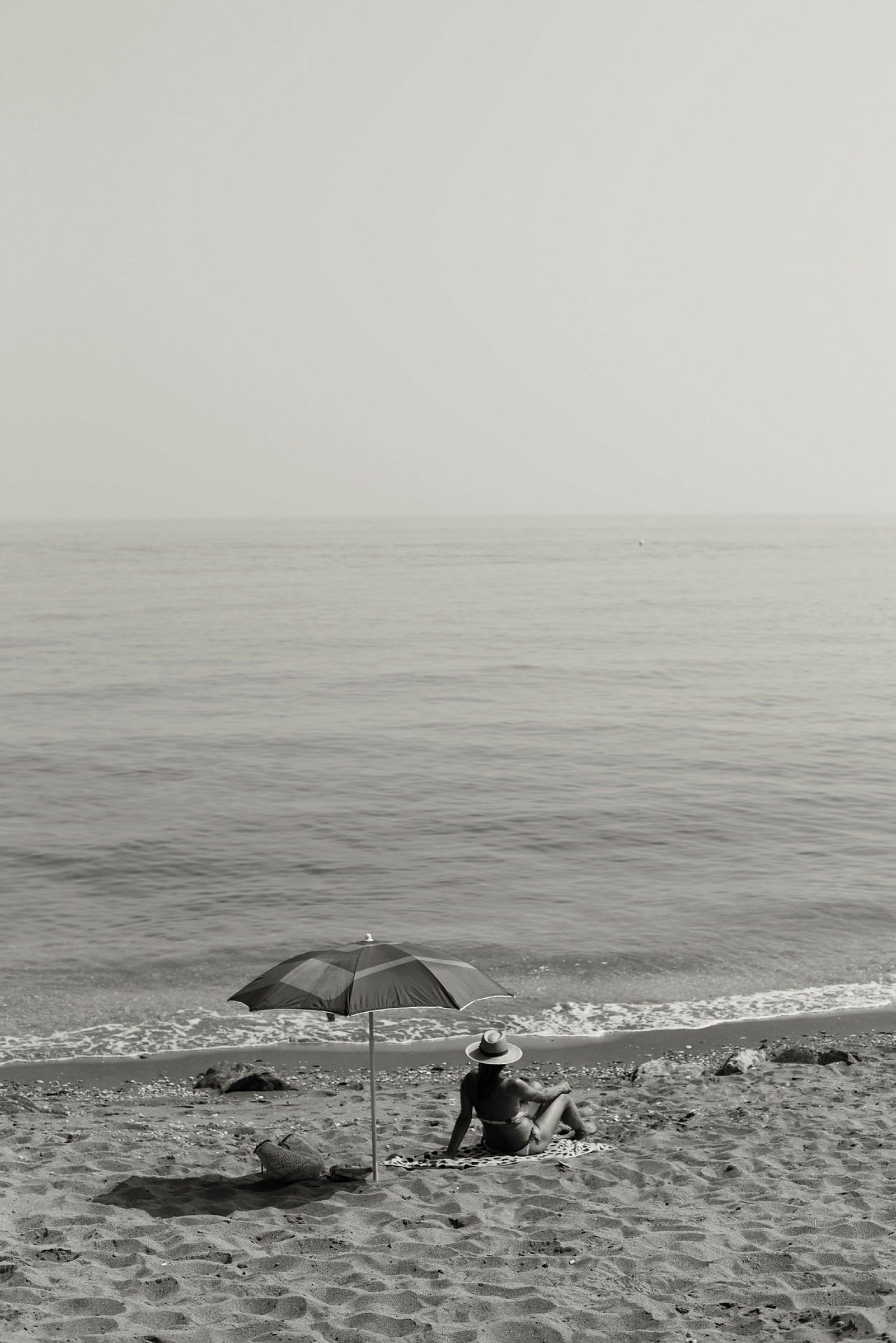 En person sitter under ett parasoll på en sandstrand nära havet. (AI-genererad text)