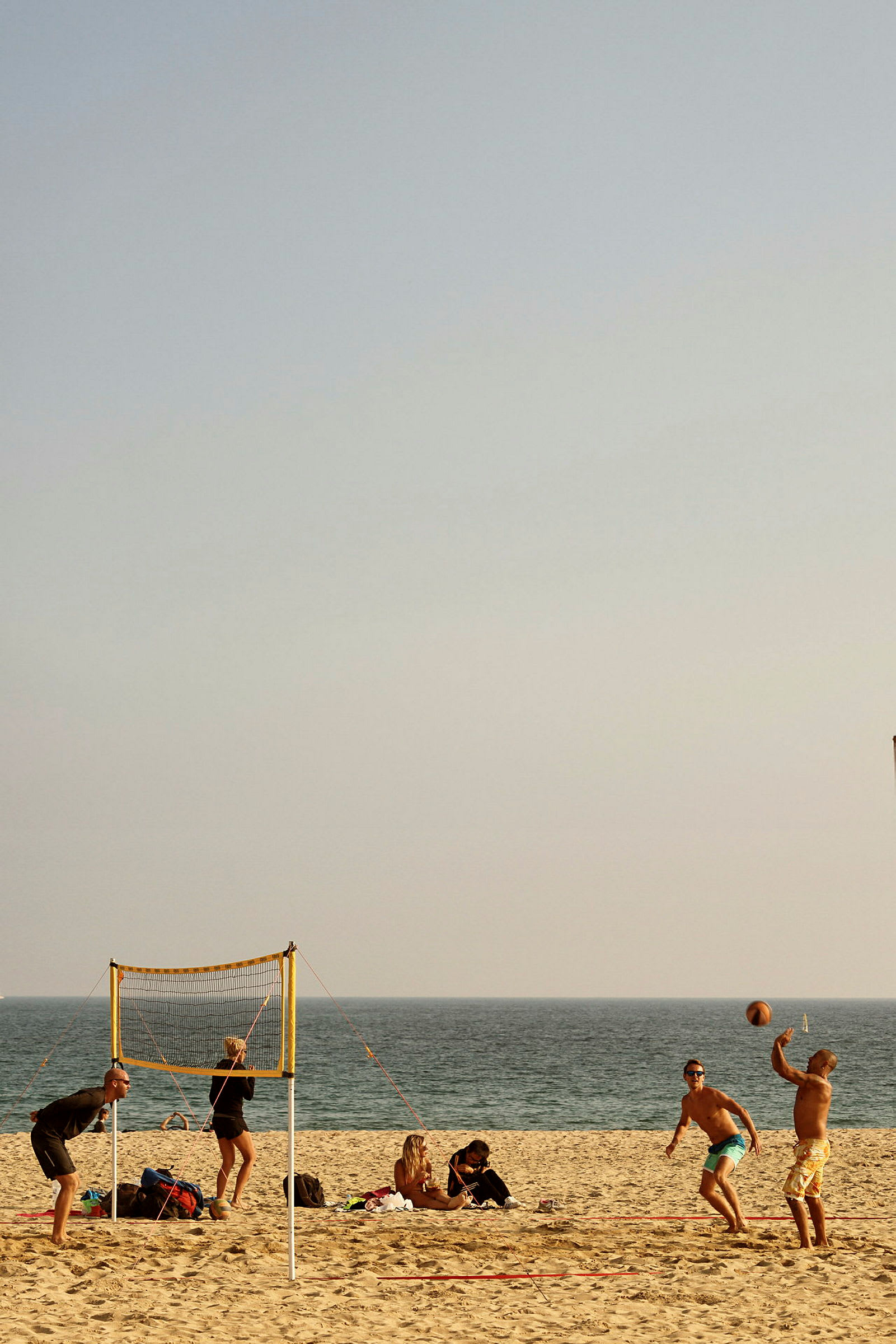 En grupp människor spelar volleyboll på en sandstrand nära havet. (AI-genererad text)
