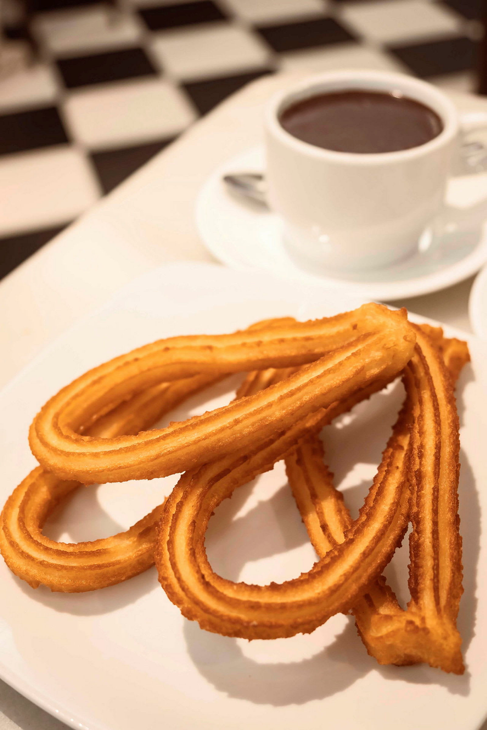 En tallrik med churros bredvid en kopp varm dryck. (AI-genererad text)