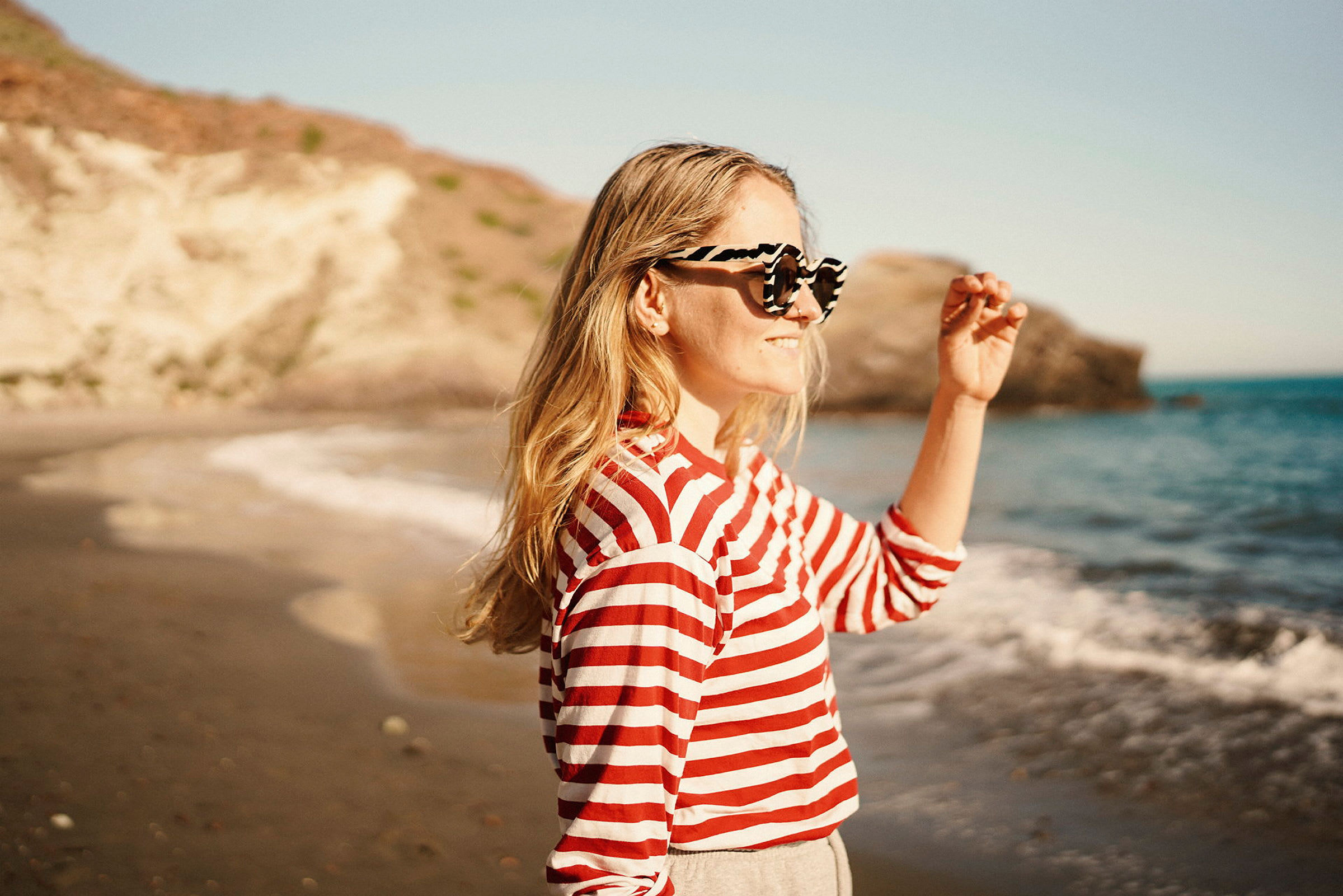 Person står vid en strand med berg i bakgrunden och havet syns. (AI-genererad text)