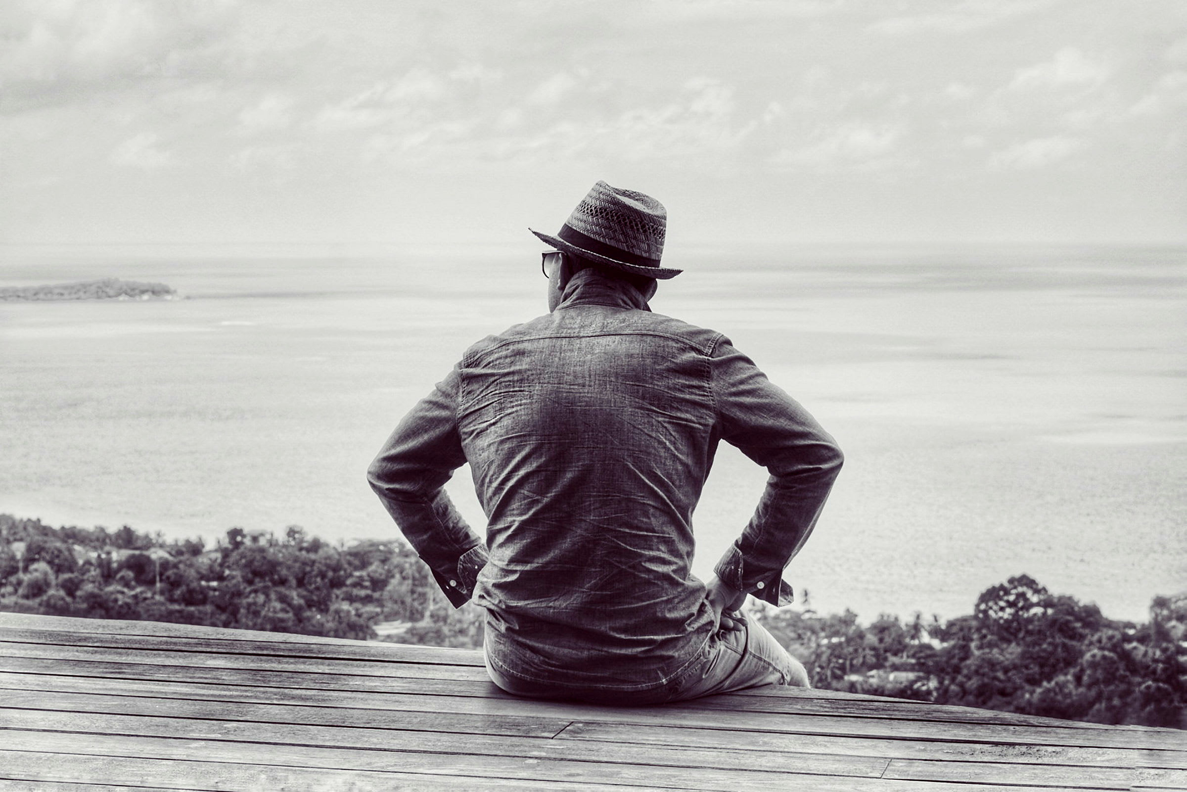 En person sittande på en träplattform med utsikt över havet. (AI-genererad text)
