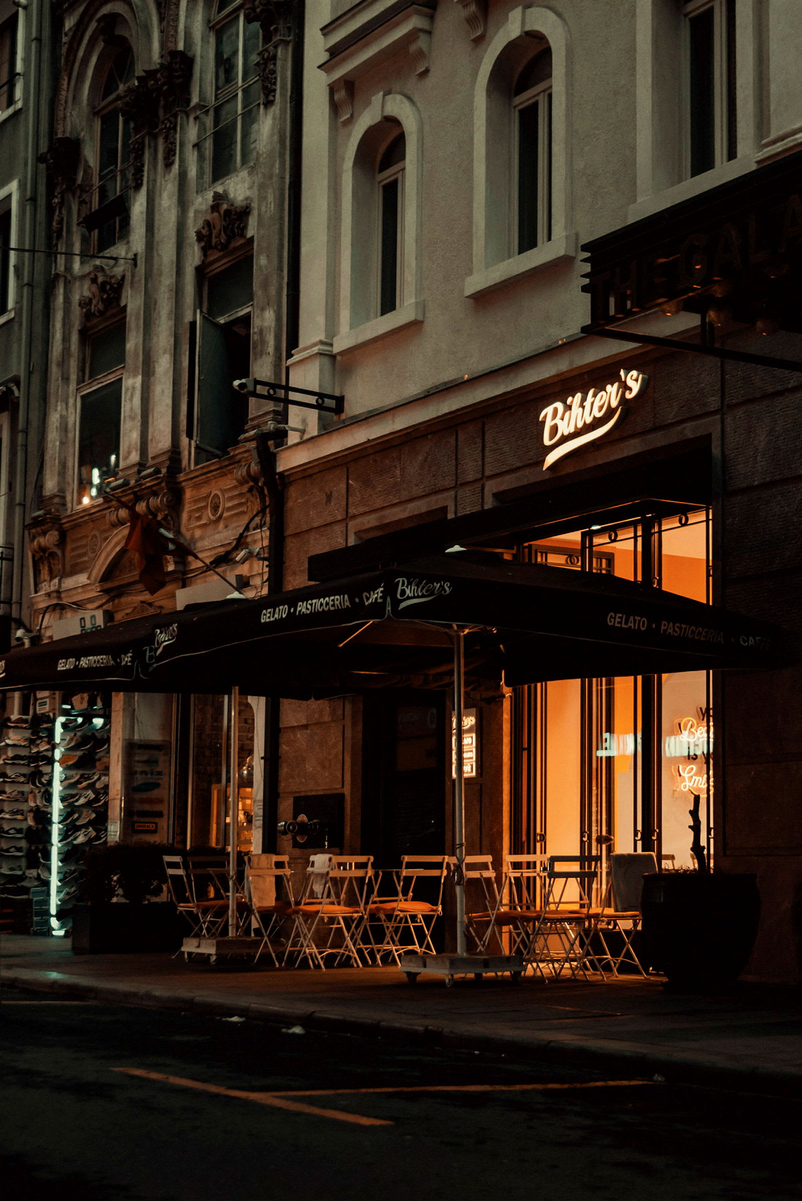 En cafébyggnad med uteservering och markiser, belyst under kvällen. (AI-genererad text)