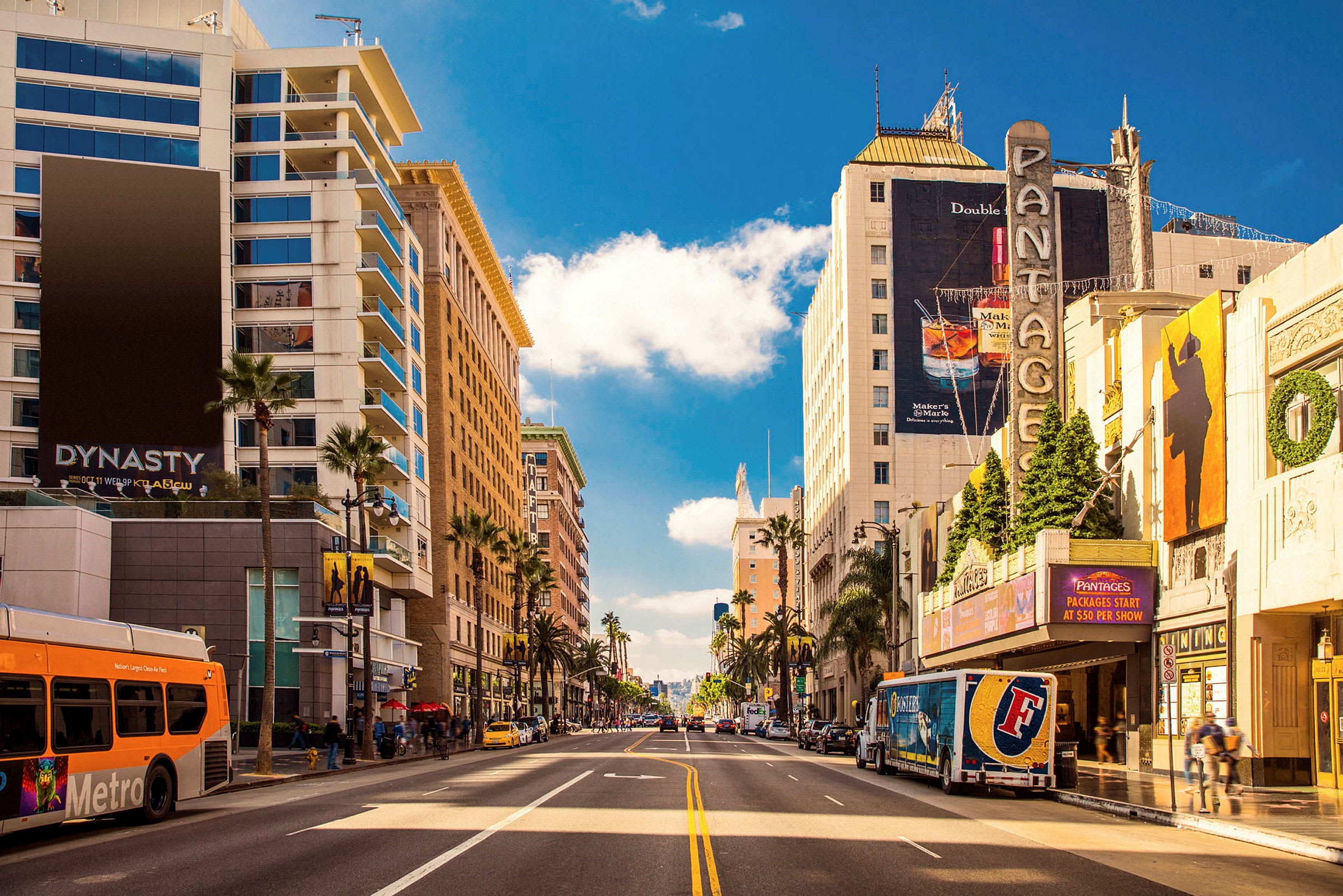 En stadsgata kantad av höga byggnader, palmer och affischer, med trafikerad väg och bilar. (AI-genererad text)
