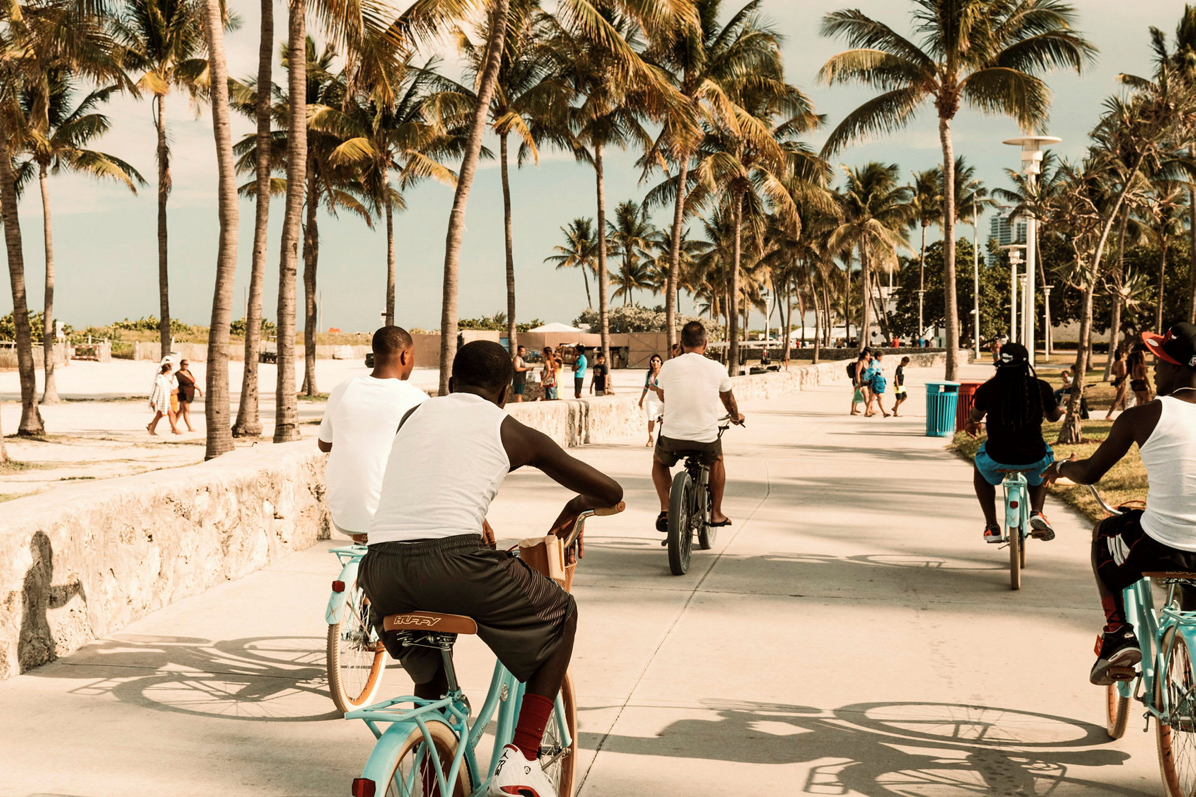 Personer cyklar på en strandpromenad omgiven av palmer. (AI-genererad text)