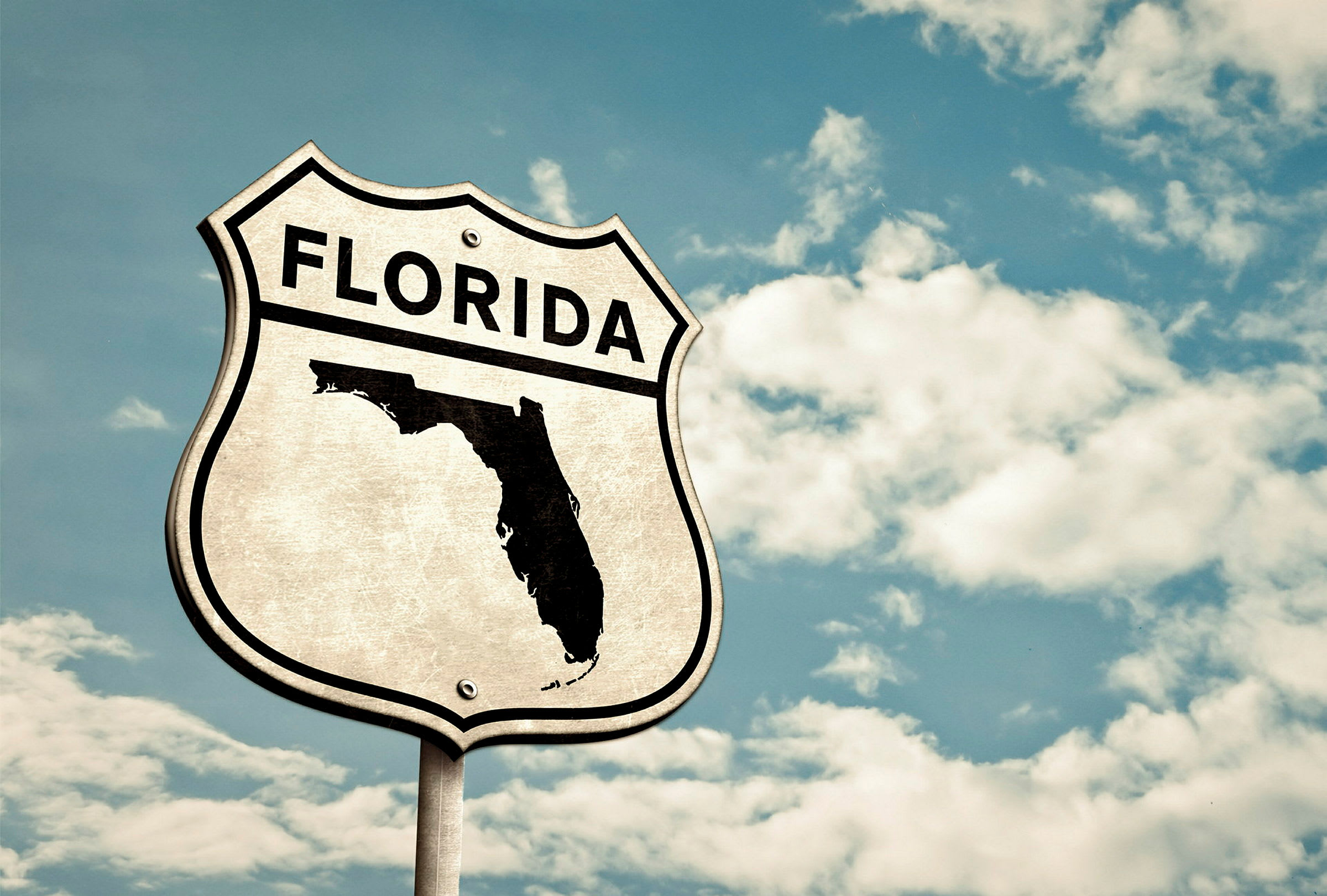 Skylt med texten 'Florida' och silhuetten av delstaten mot en blå himmel med vita moln. (AI-genererad text)