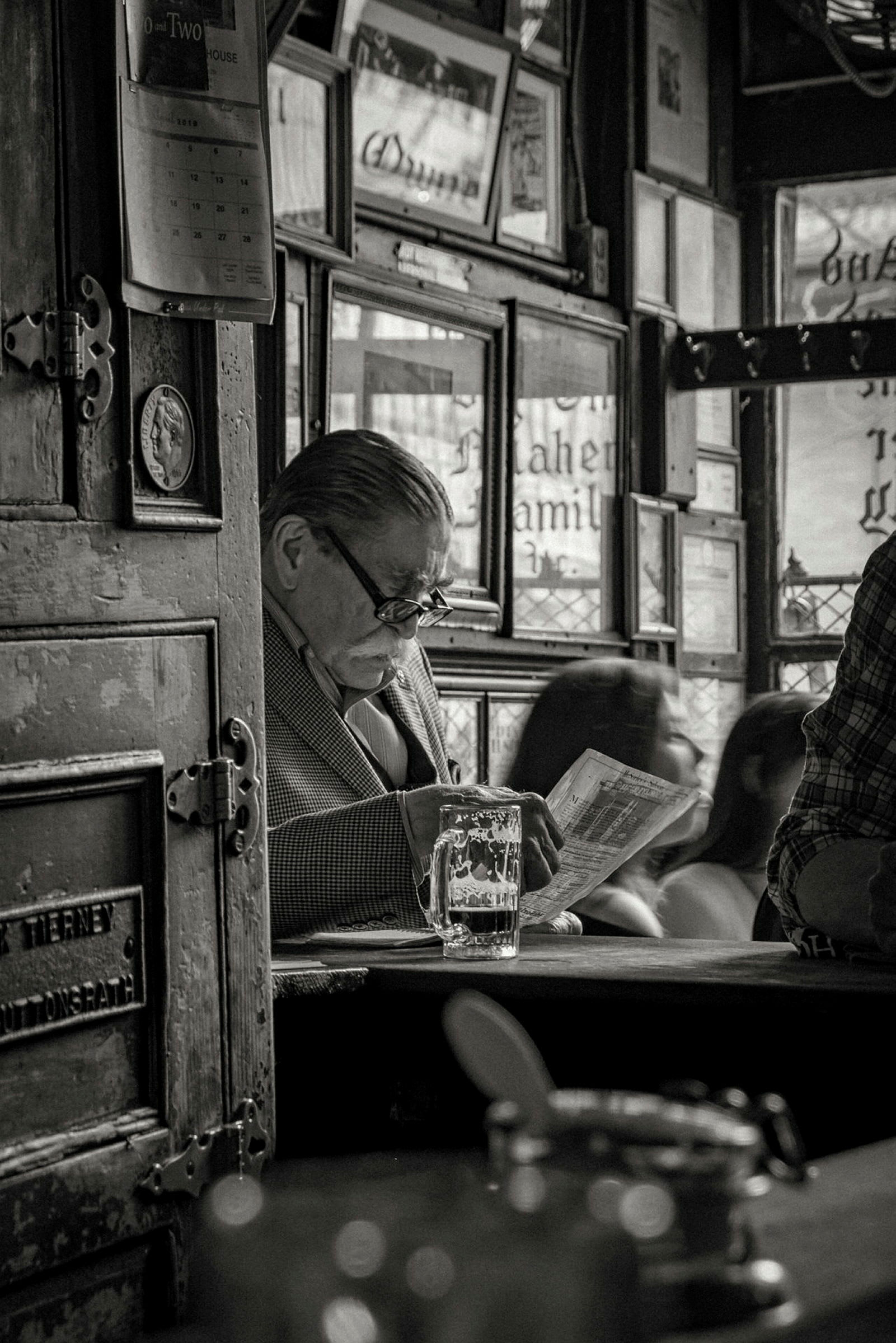 Interiör av en pub med en glas öl placerad på en bar och en person som läser en tidning. (AI-genererad text)