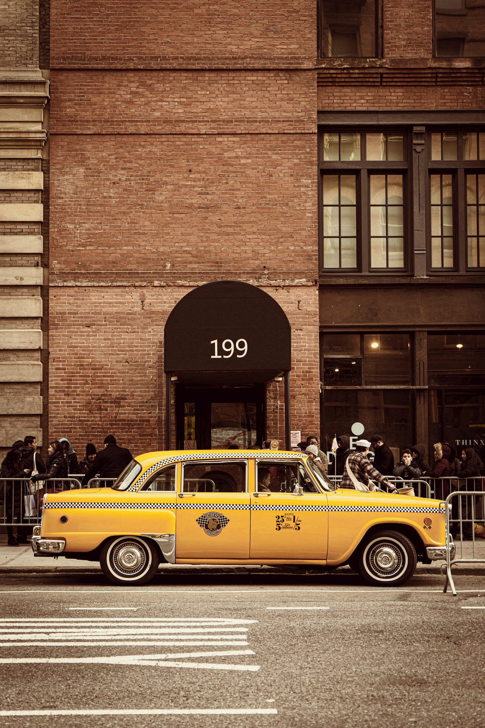 En klassisk gul taxi står parkerad framför en tegelbyggnad med nummer 199 ovanför dörren. (AI-genererad text)