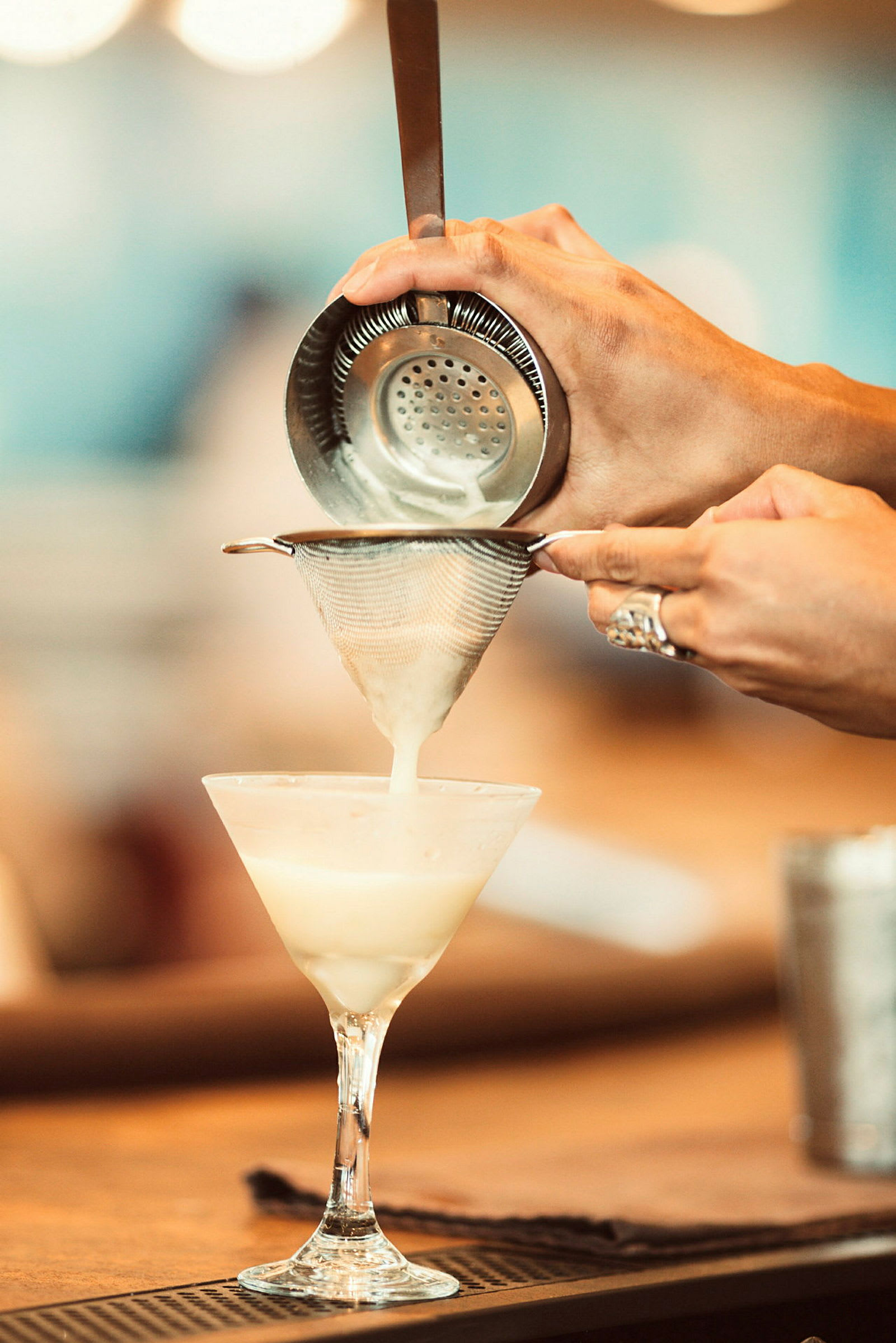 Någon silar en vit dryck i ett cocktailglas. (AI-genererad text)
