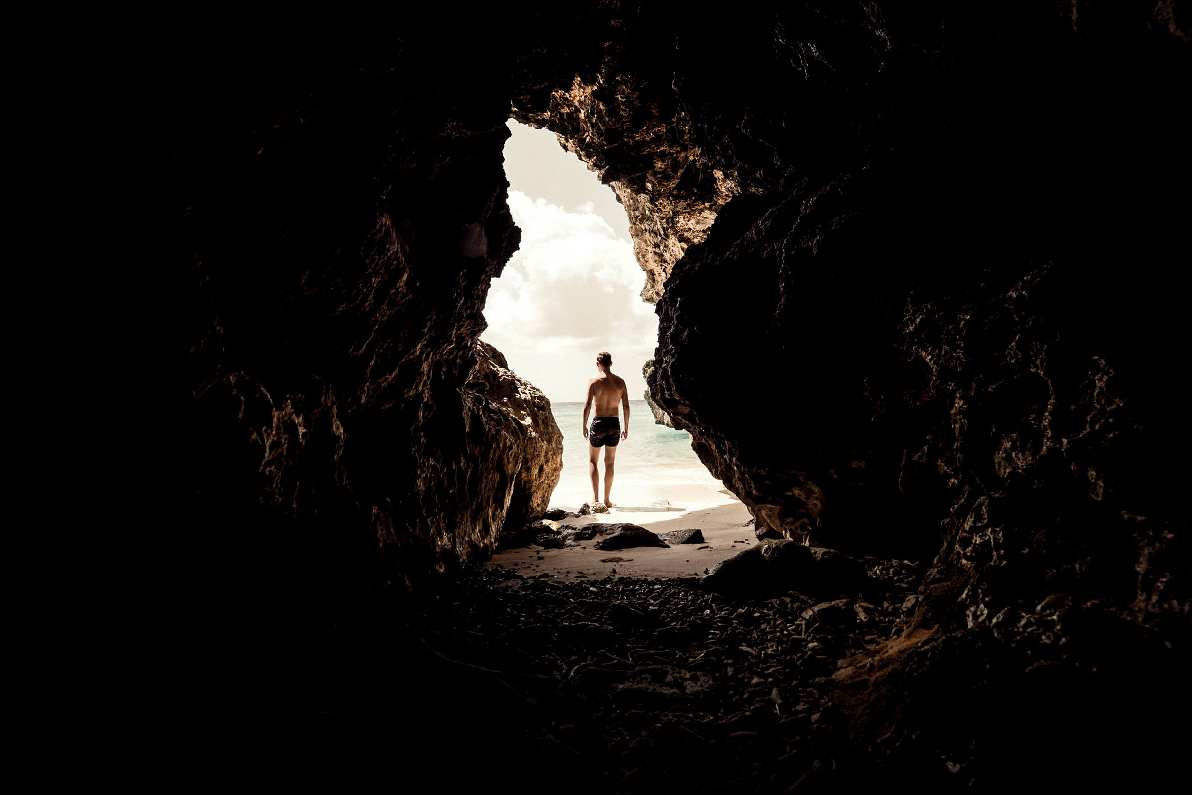En person står vid öppningen av en mörk grotta med utsikt mot havet. (AI-genererad text)