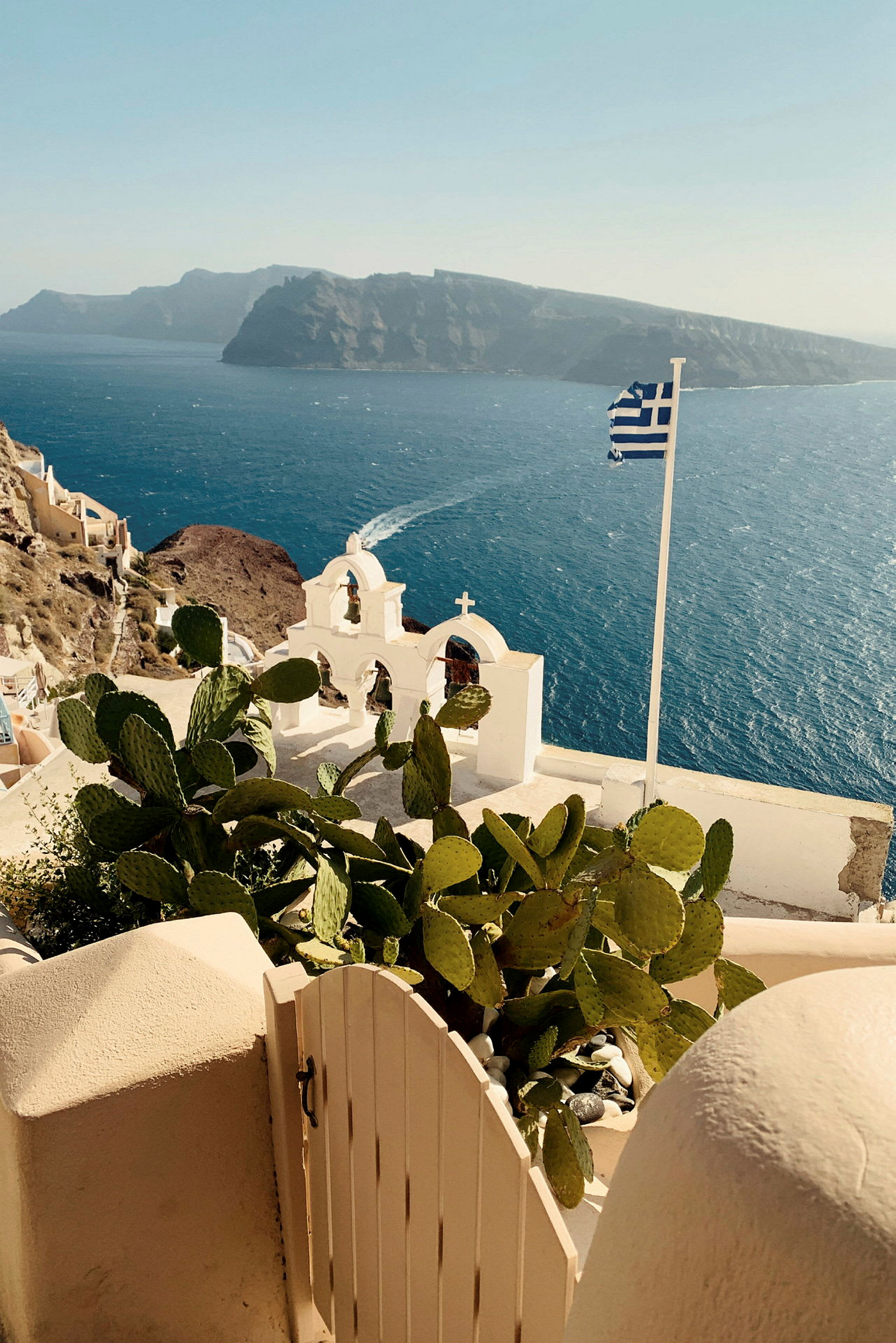 Vy över Santorini med blått hav, vit kyrka och grekisk flagga. (AI-genererad text)