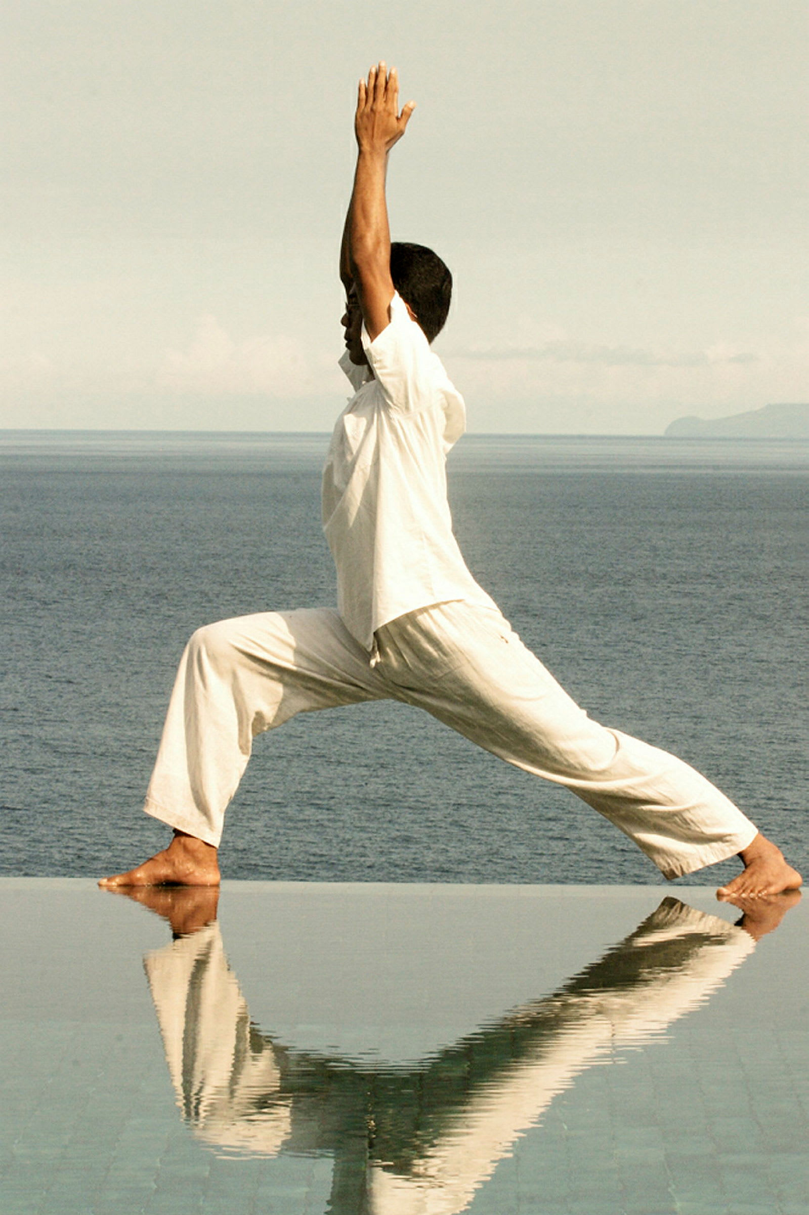 En person utför en yogaposition vid en vattenyta med havet i bakgrunden. (AI-genererad text)