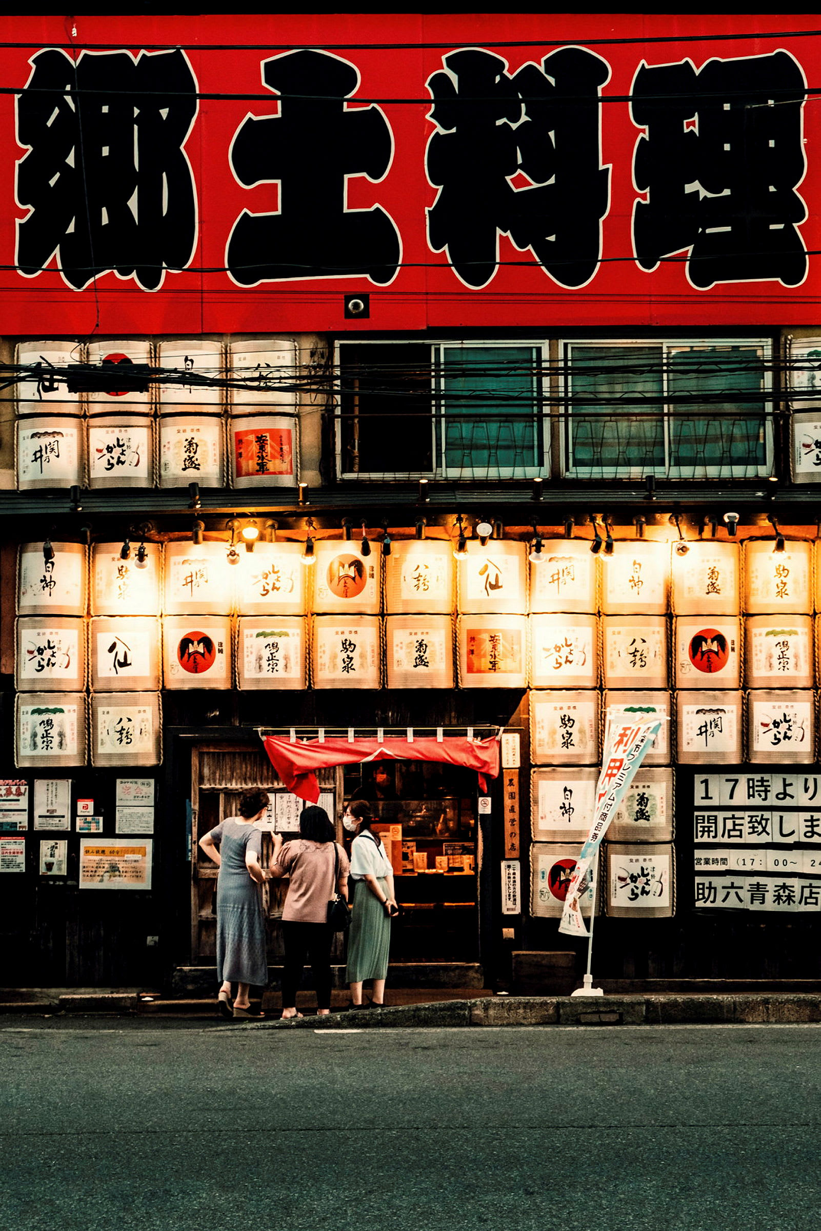Fasaden av en japansk restaurang med stora tecken och lanternor, samt några personer ståendes utanför. (AI-genererad text)