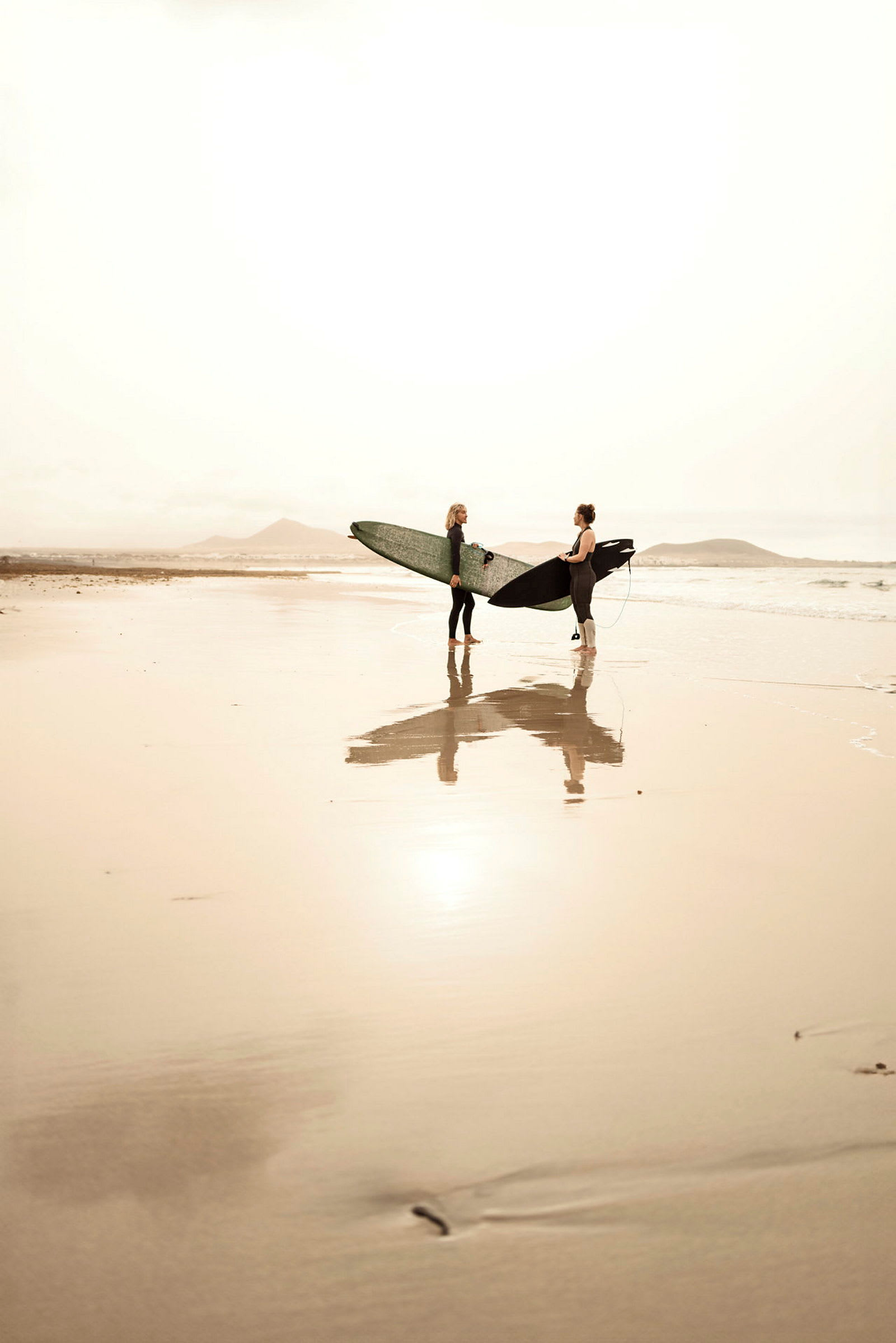 Två personer står med surfingbrädor på en solig strand. (AI-genererad text)
