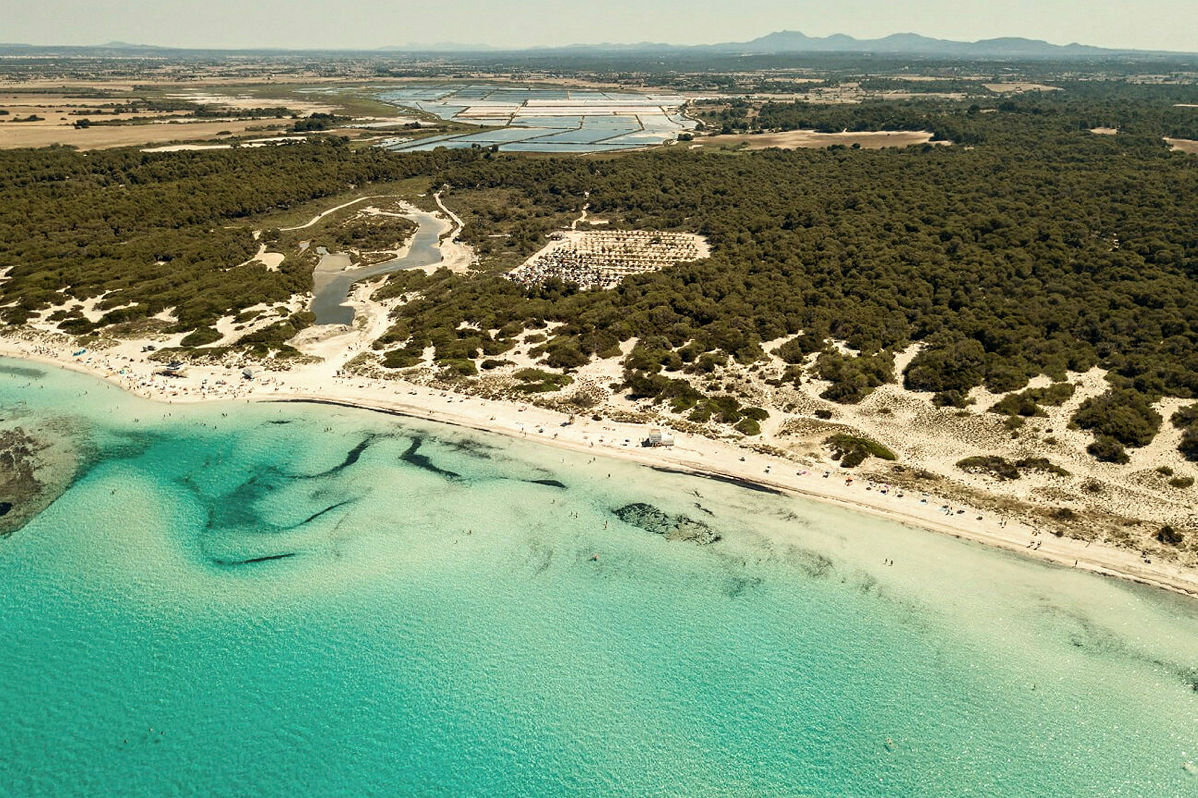 Flygfoto av en strand med klart turkost vatten och omgivande skog. (AI-genererad text)