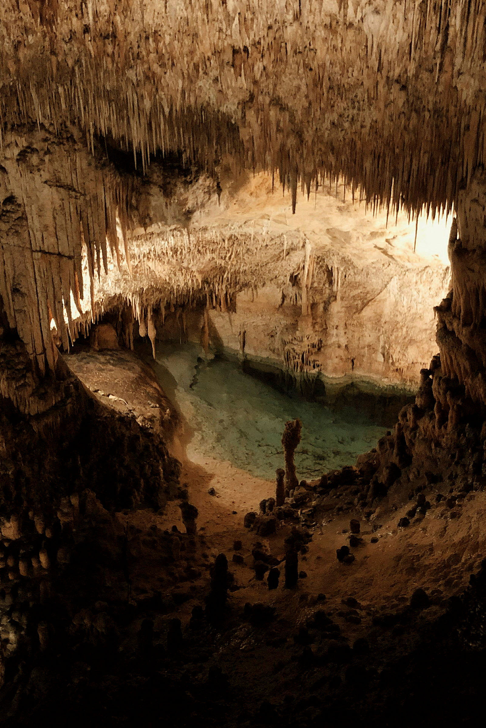 Bild av en grotta med stalaktiter i taket, stalagmiter på marken och en klar vattenpool. (AI-genererad text)