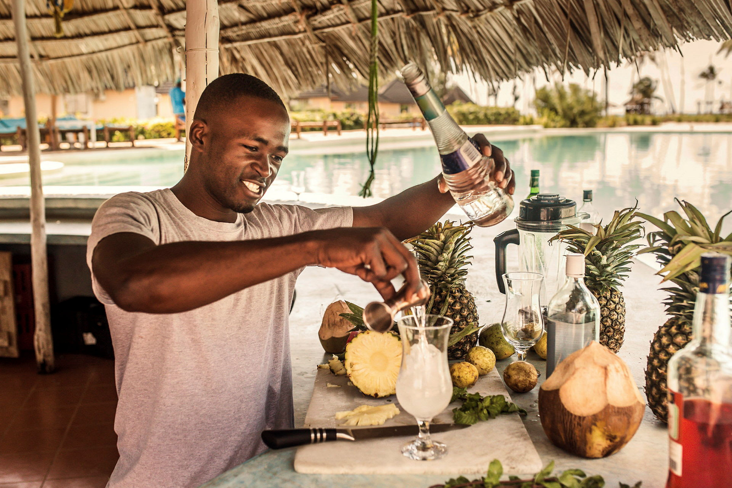 En person tillreder en drink vid en poolbar med färska frukter och drycker. (AI-genererad text)