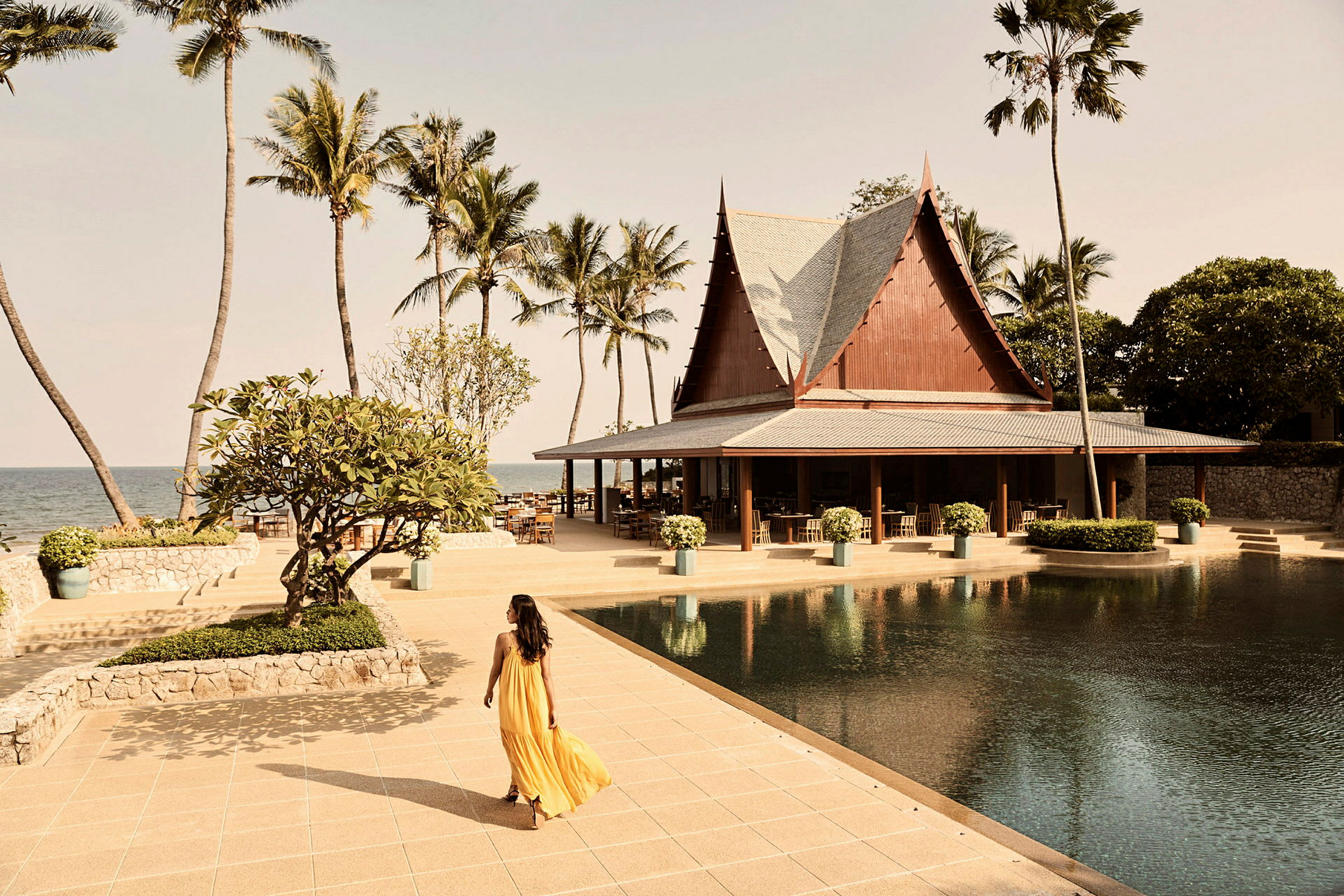 Resort med traditionell byggnad, palmer och pool nära havet. (AI-genererad text)