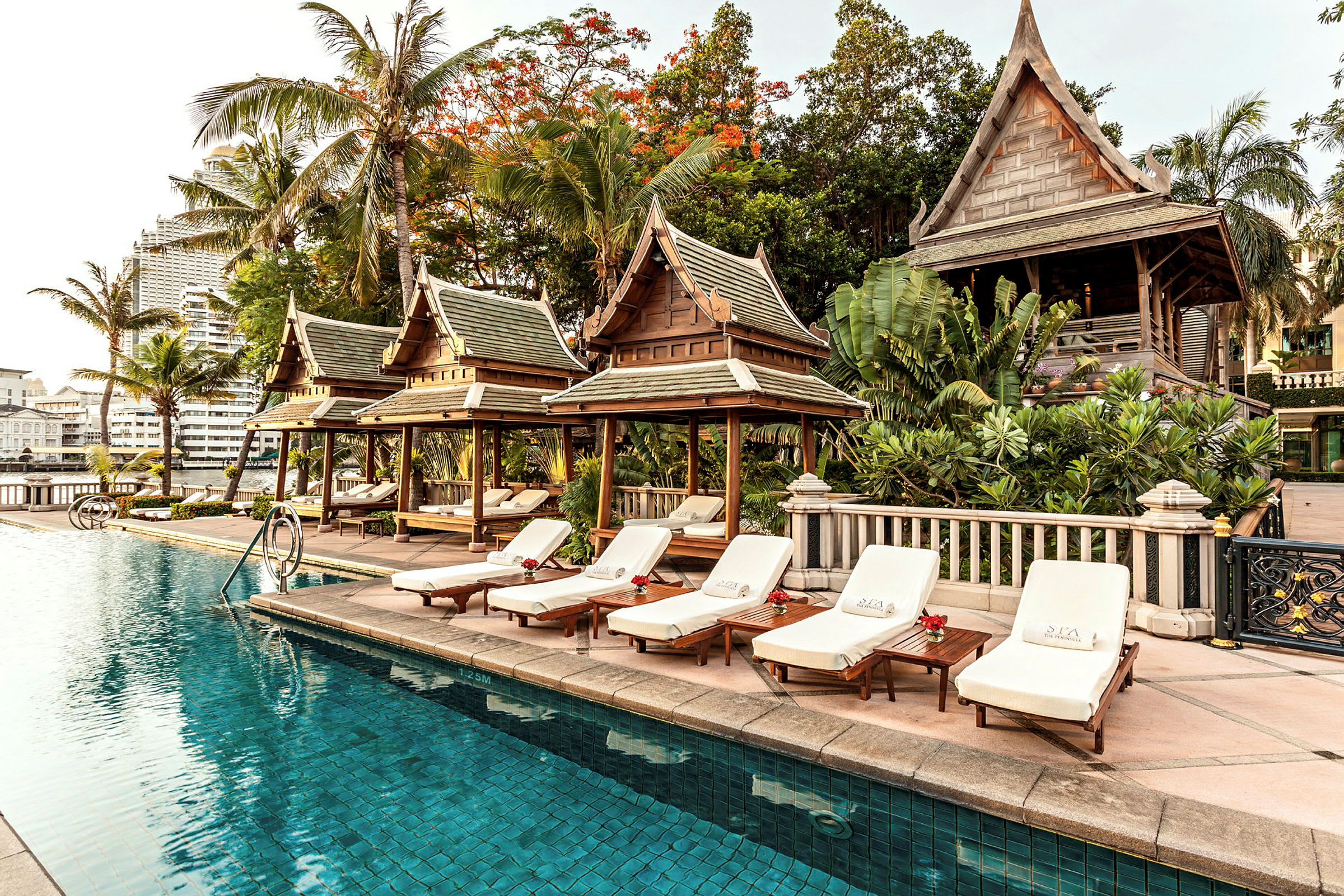 Solstolar vid en pool med traditionella thailändska paviljonger och grönt område. (AI-genererad text)