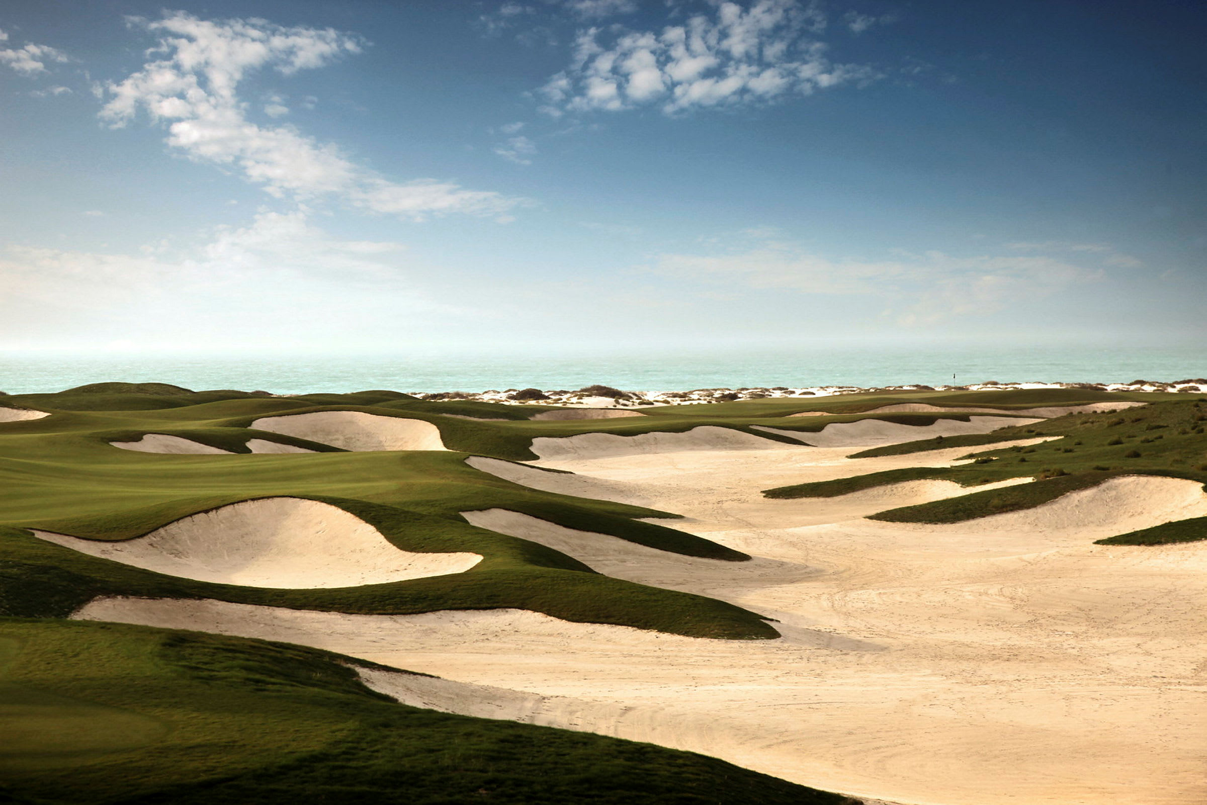 Golfbana med gröna ytor och sandbunkrar vid gränsen till havet. (AI-genererad text)
