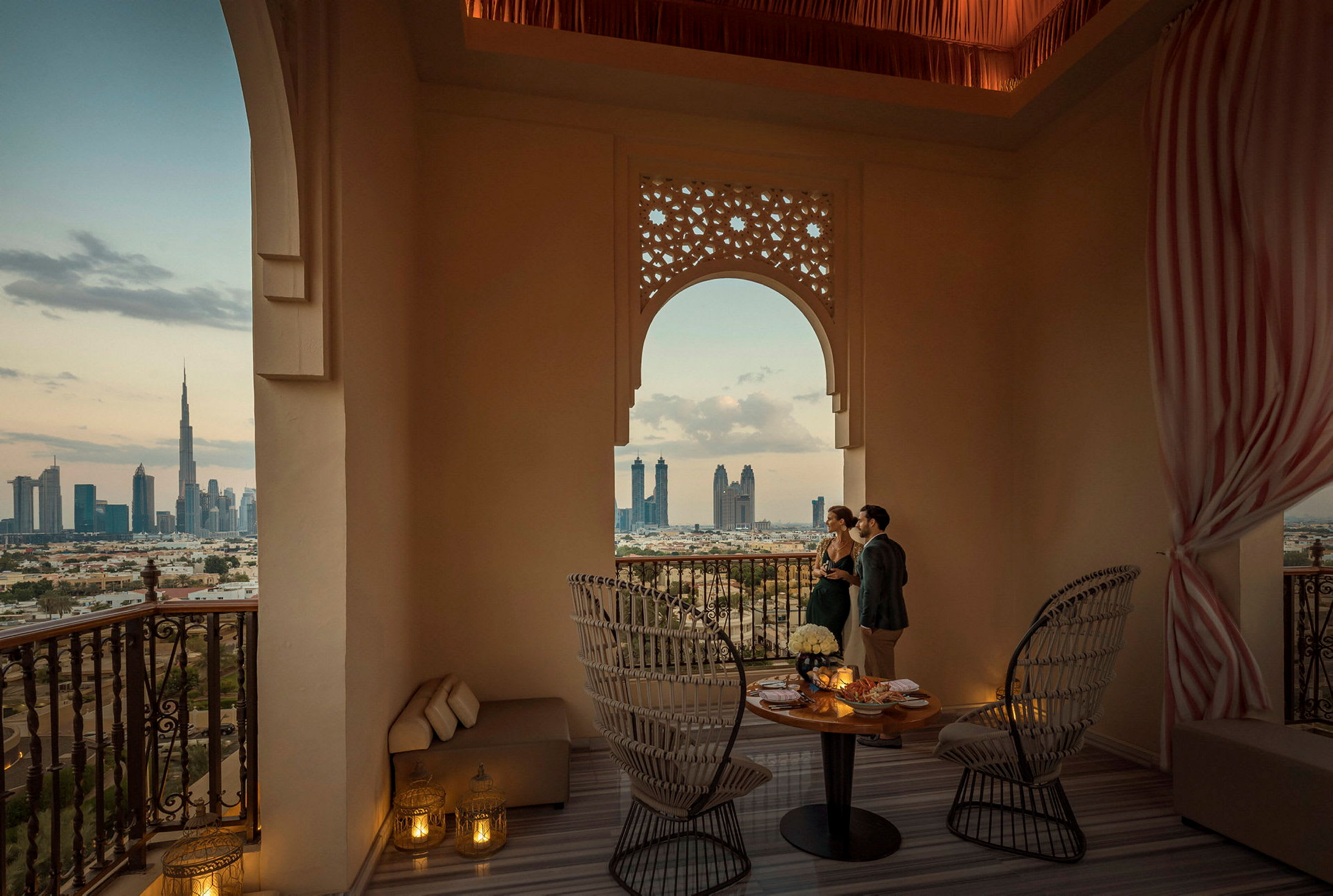 Vy över Dubai från en elegant inredd balkong med bord och stolar. (AI-genererad text)
