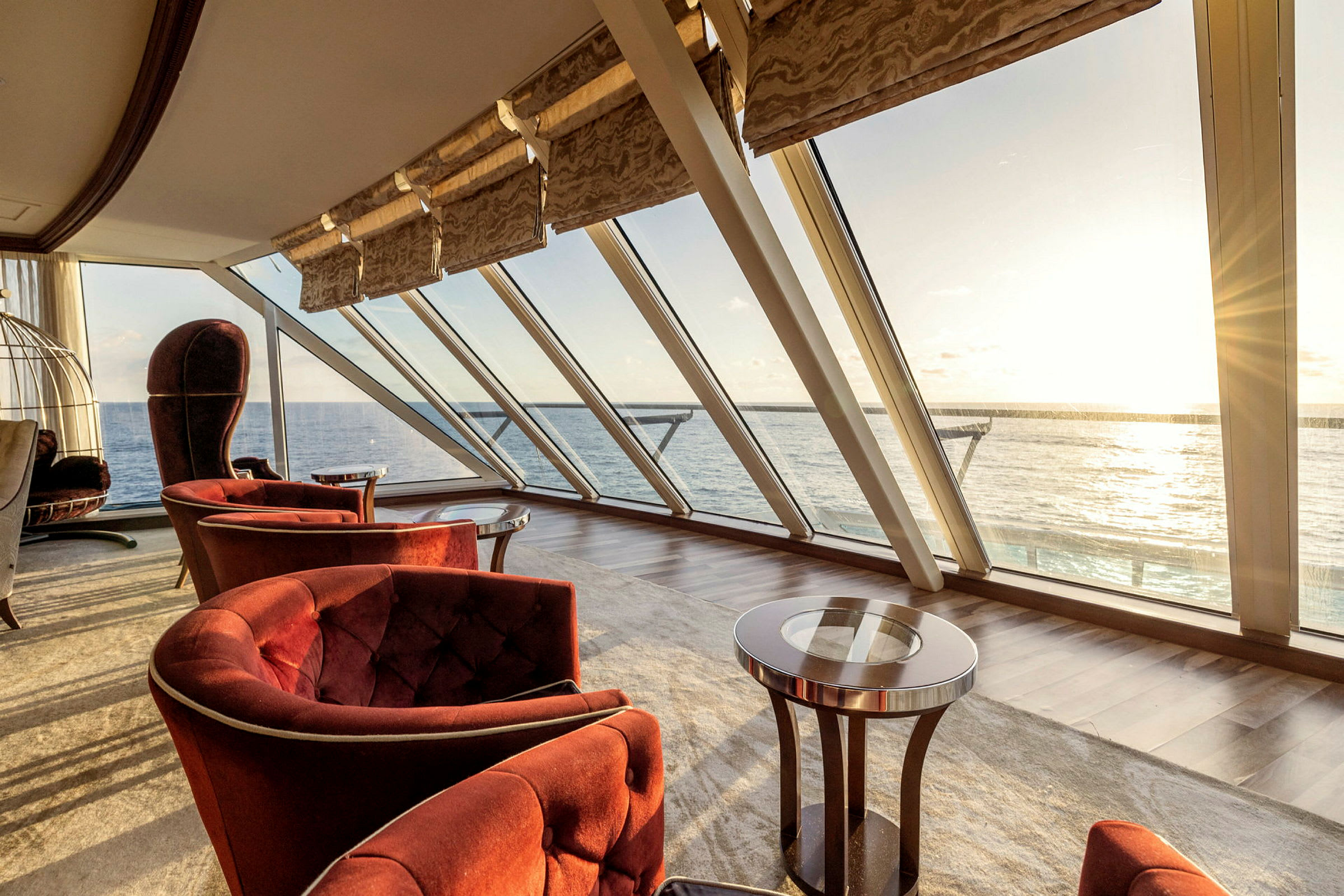 En elegant lounge med röda fåtöljer vid stora fönster mot havet under solnedgång. (AI-genererad text)