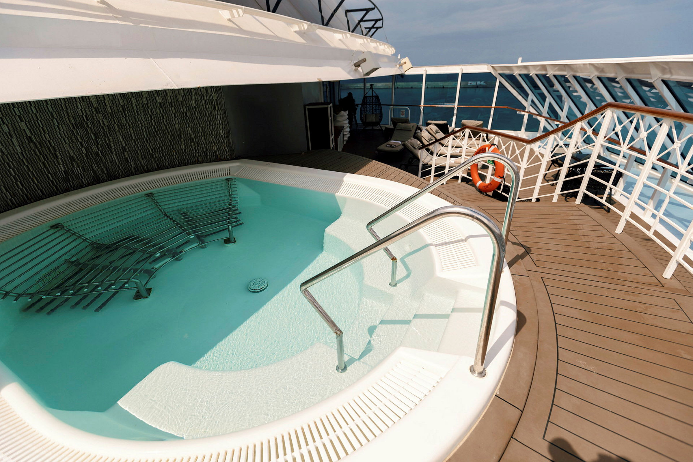 En jacuzzi med metallräcken, omgiven av ett trädäck och stolar på ett kryssningsfartyg. (AI-genererad text)