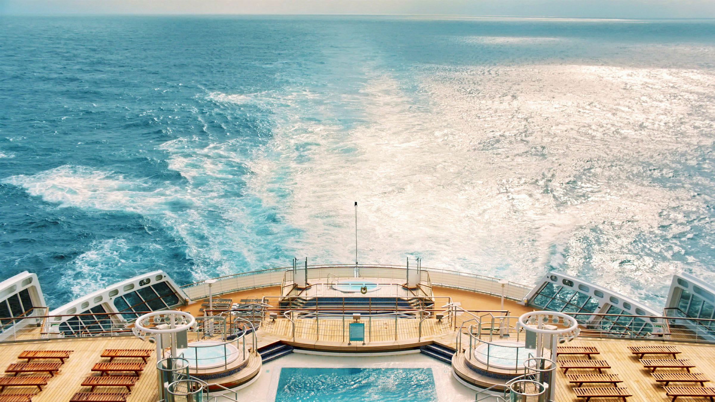 Bakdäck på ett kryssningsfartyg med bubbelpooler och solstolar, havet synligt i bakgrunden. (AI-genererad text)