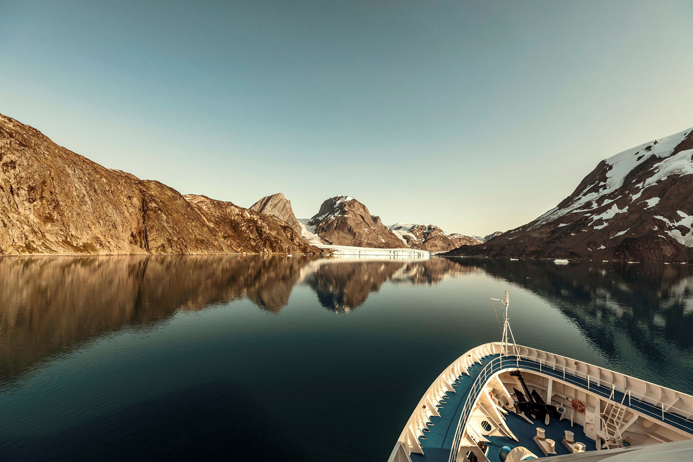 Ett fartyg i en lugn fjord omgiven av berg med snö. (AI-genererad text)